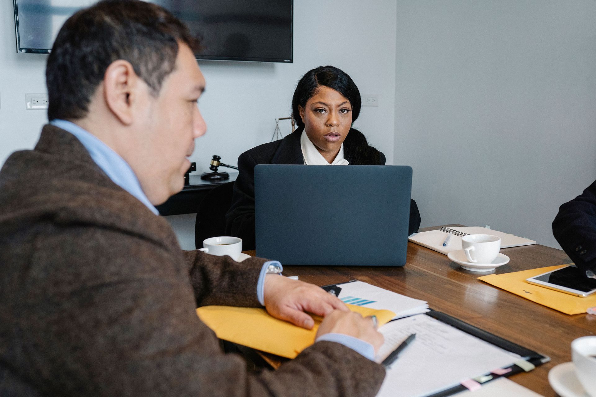 Meeting room with three people, laptop, papers, and cups on a conference table