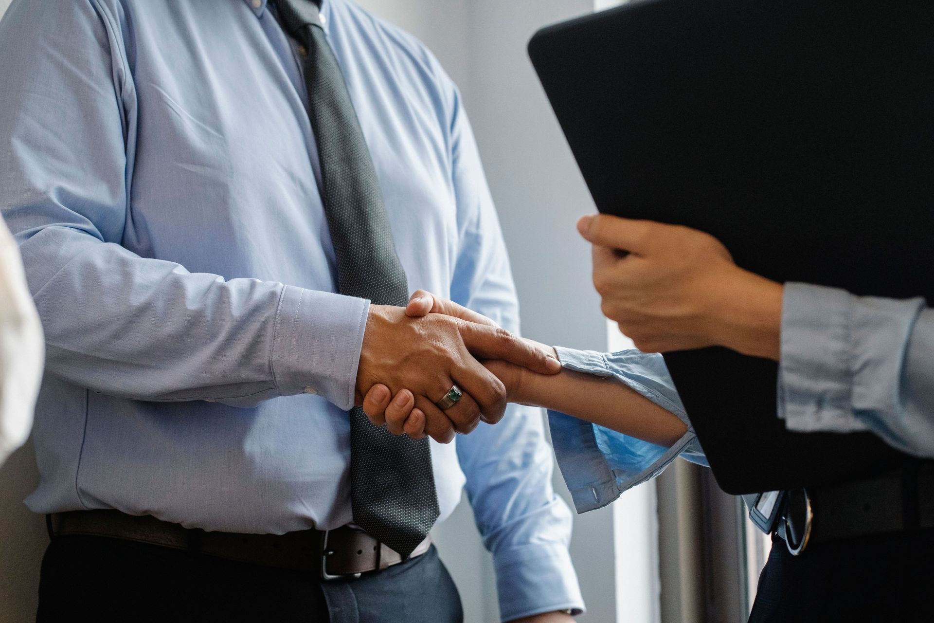 Two people in dress shirts shaking hands, with one holding a black folder