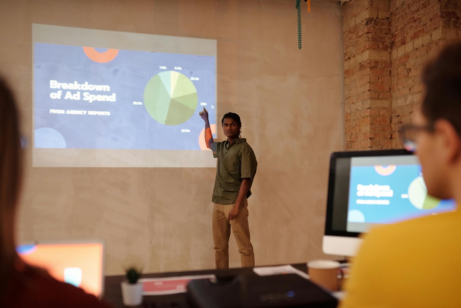 A person presents a pie chart about ad spending to a group in an office setting.