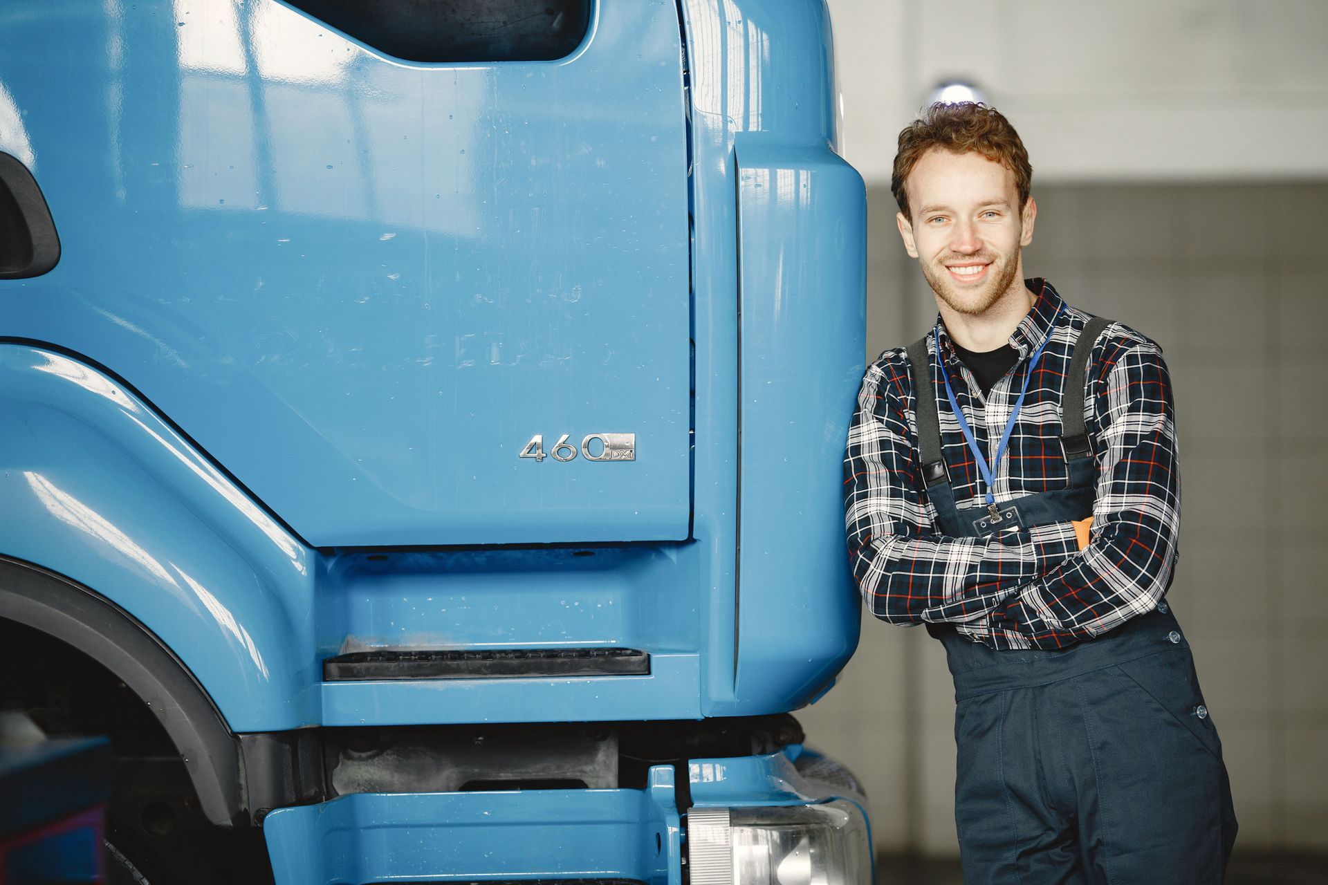 Man leaning against a blue truck in a garage, arms crossed and smiling