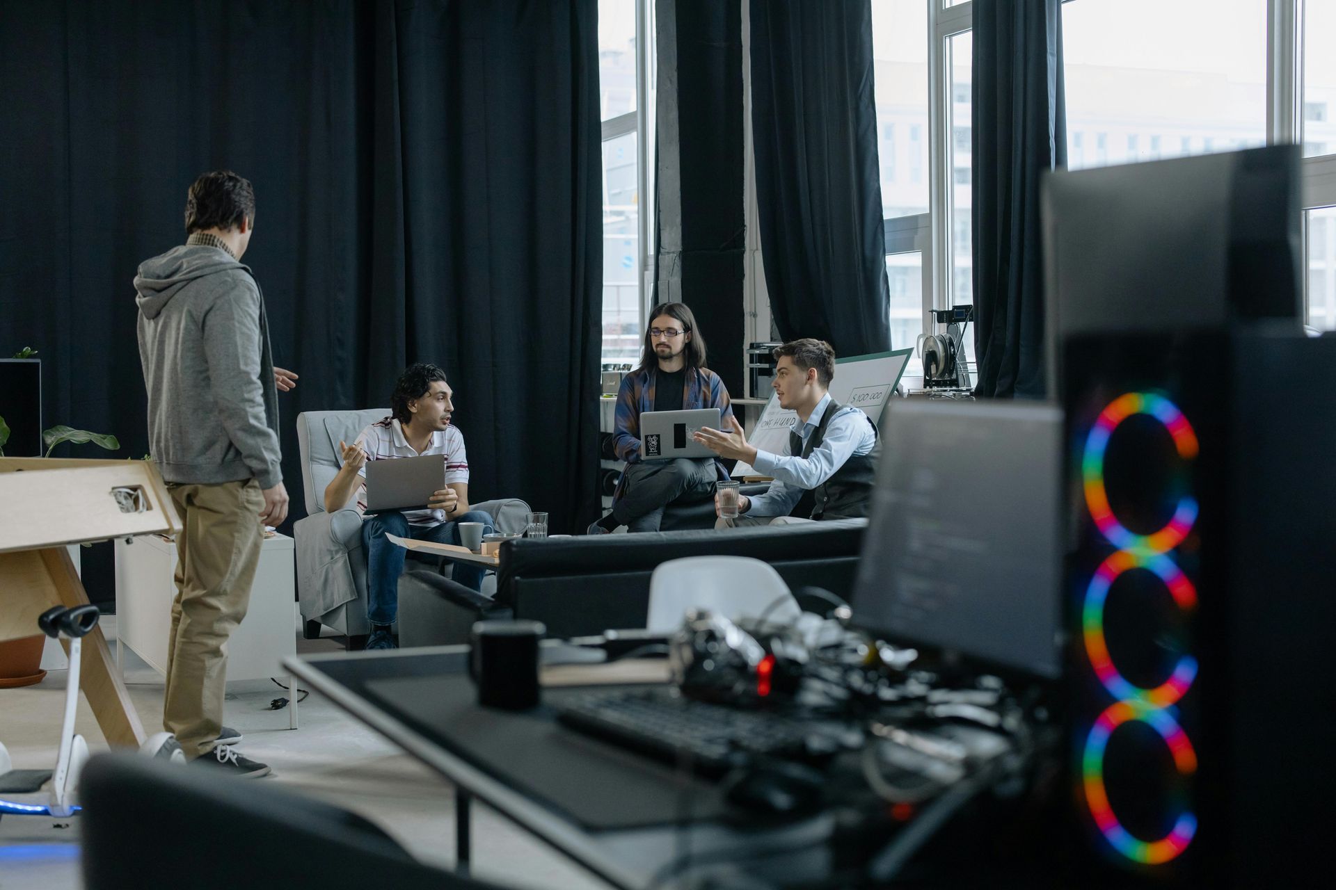Four people collaborate in a modern office space, with three seated in a lounge area and one standing nearby.
