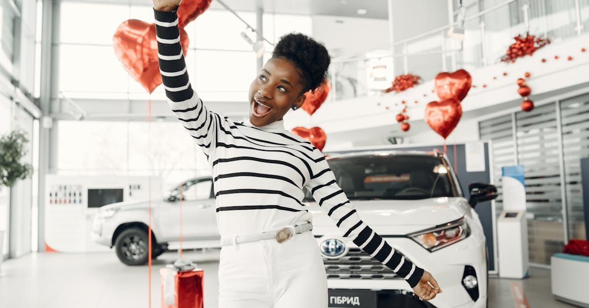 A woman is holding balloons in front of a car in a showroom.
