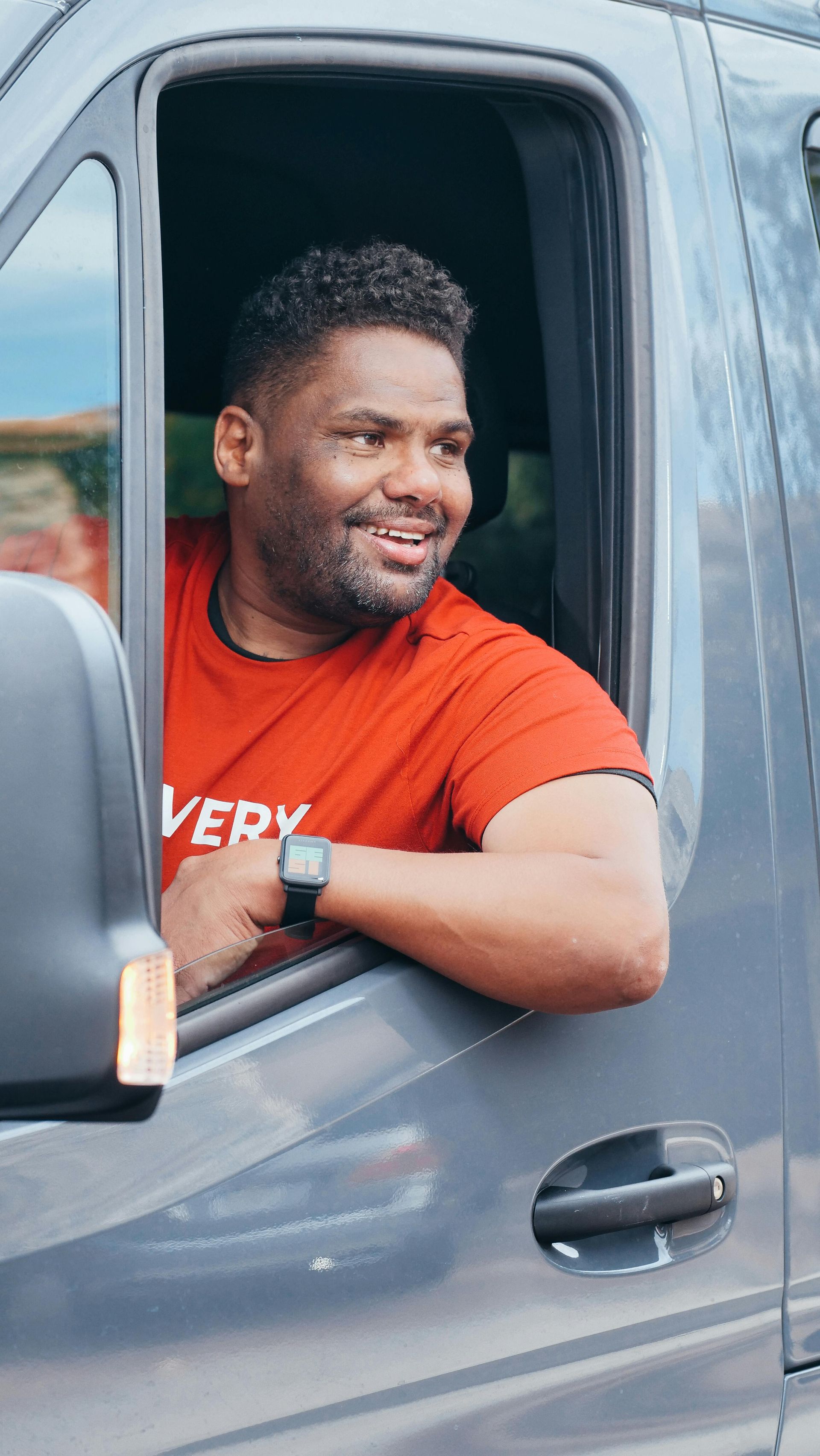 A man in a red shirt is sitting in the driver 's seat of a van.