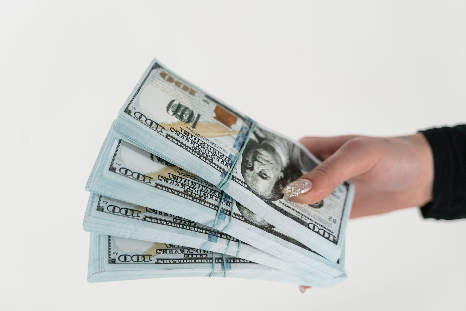 A hand holding several fanned-out $100 bills against a white background