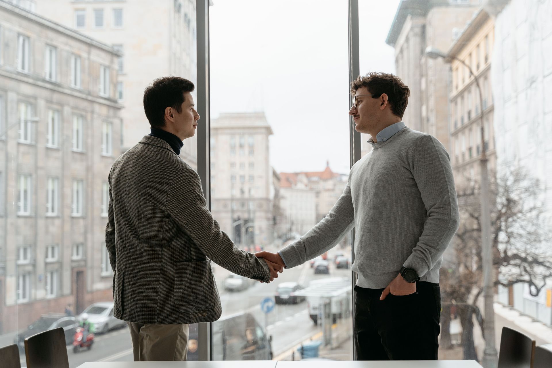 Two men shaking hands by a window overlooking a snowy city street