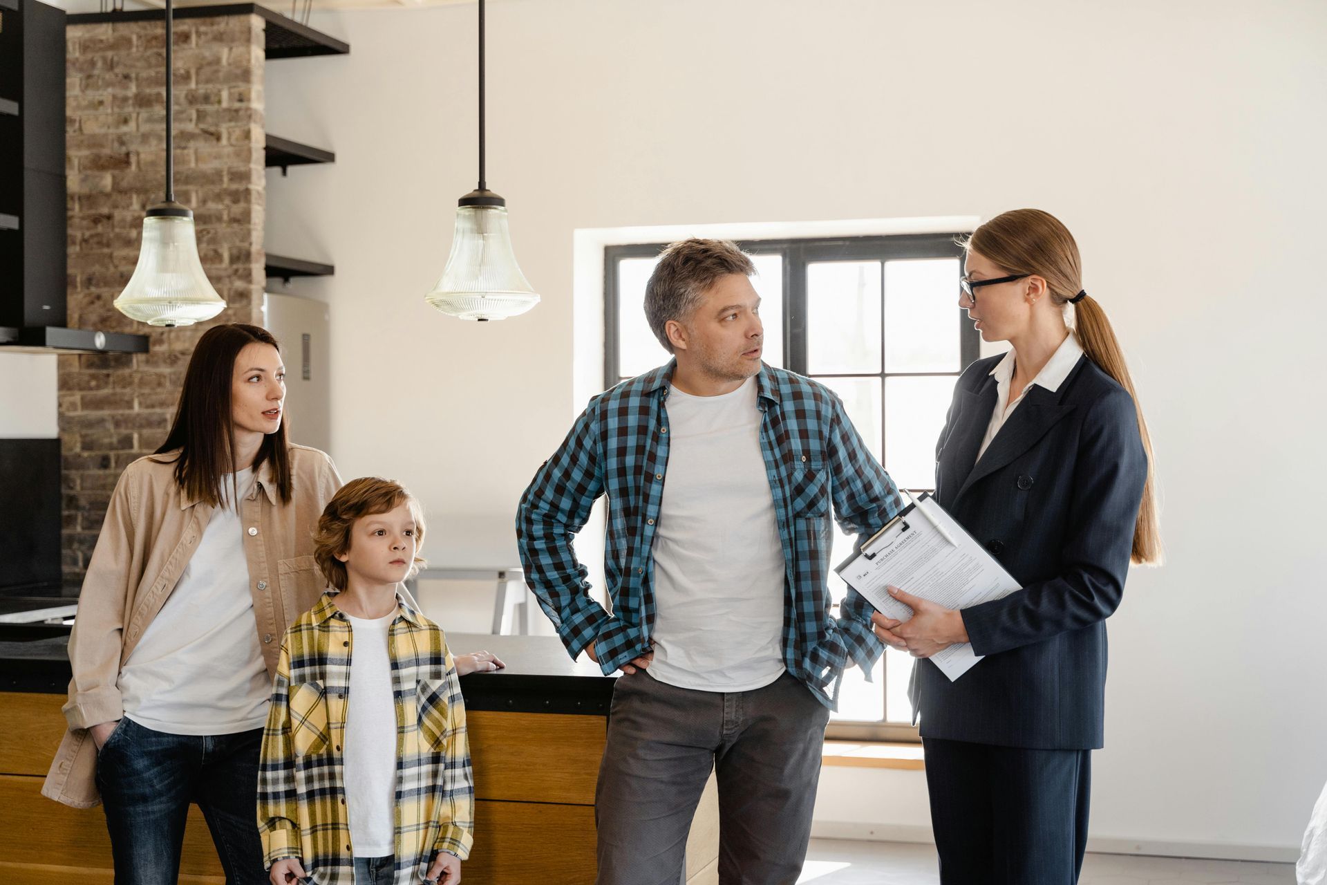 Family and real estate agent discussing a property inside a home with neutral walls, brick accents, and natural light.