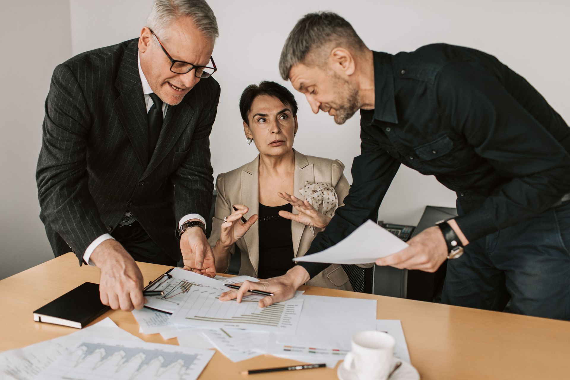 Three coworkers review charts at a table, with papers spread out and one person seated between them.