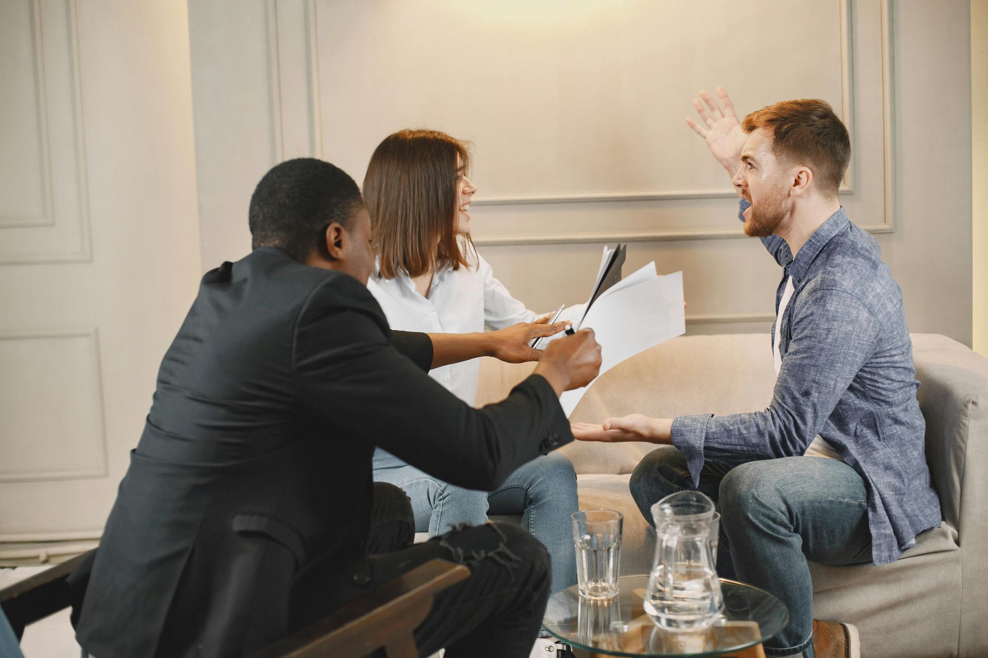 A person sits between two others in an office, gesturing while holding documents, as they engage in a heated discussion.