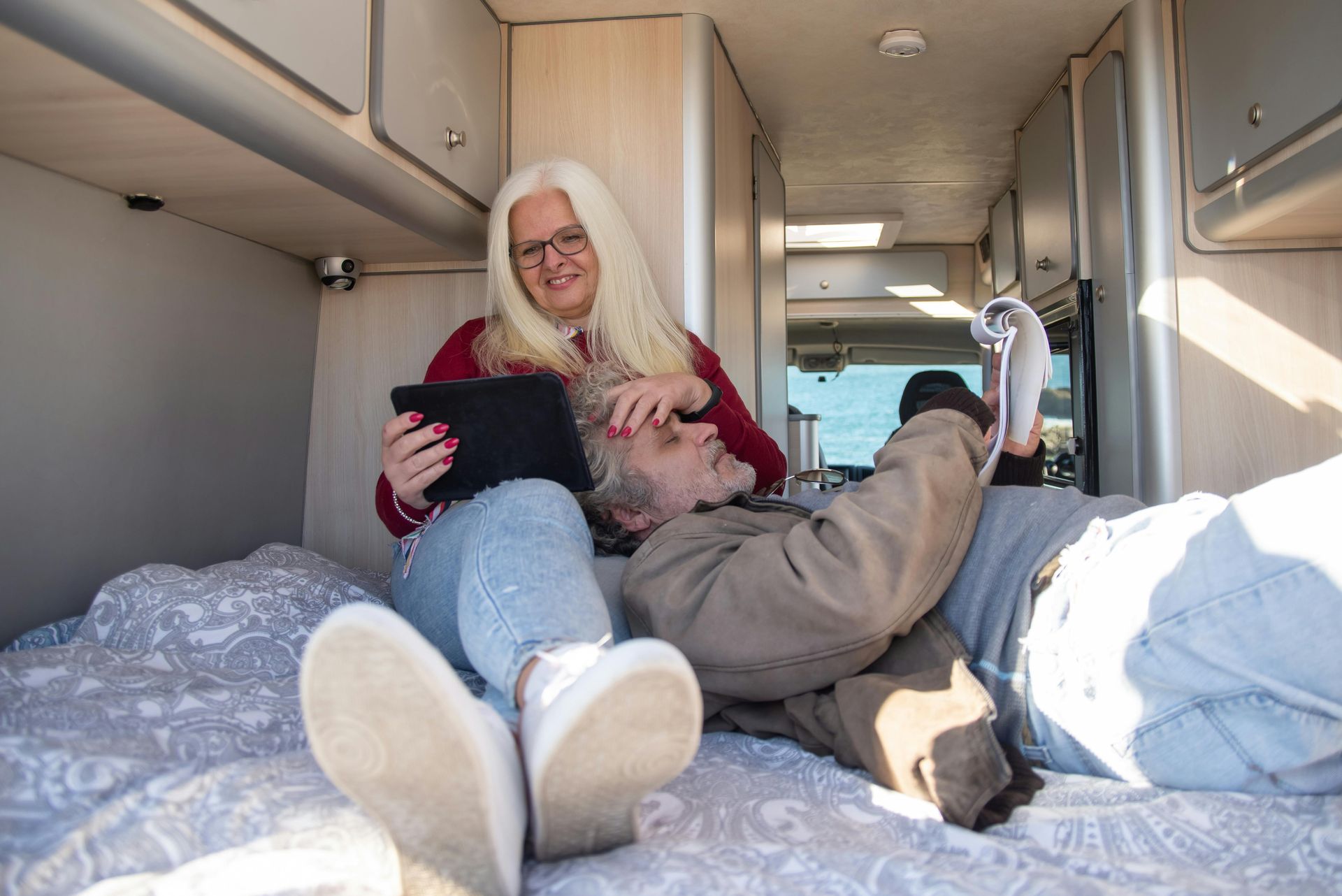 A man and a woman are laying on a bed in a camper van.