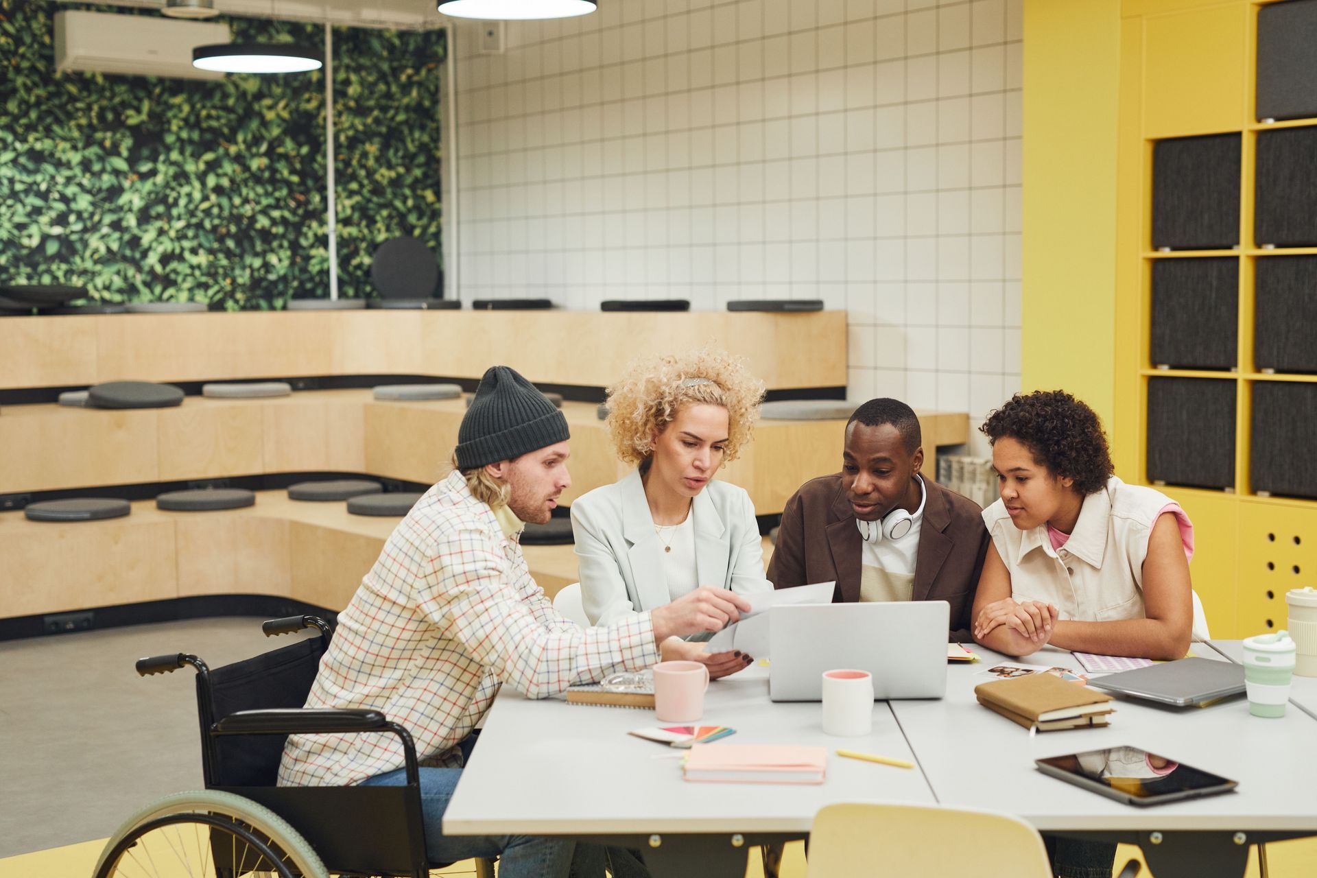 Four people collaborating at a table with a laptop in a bright modern office