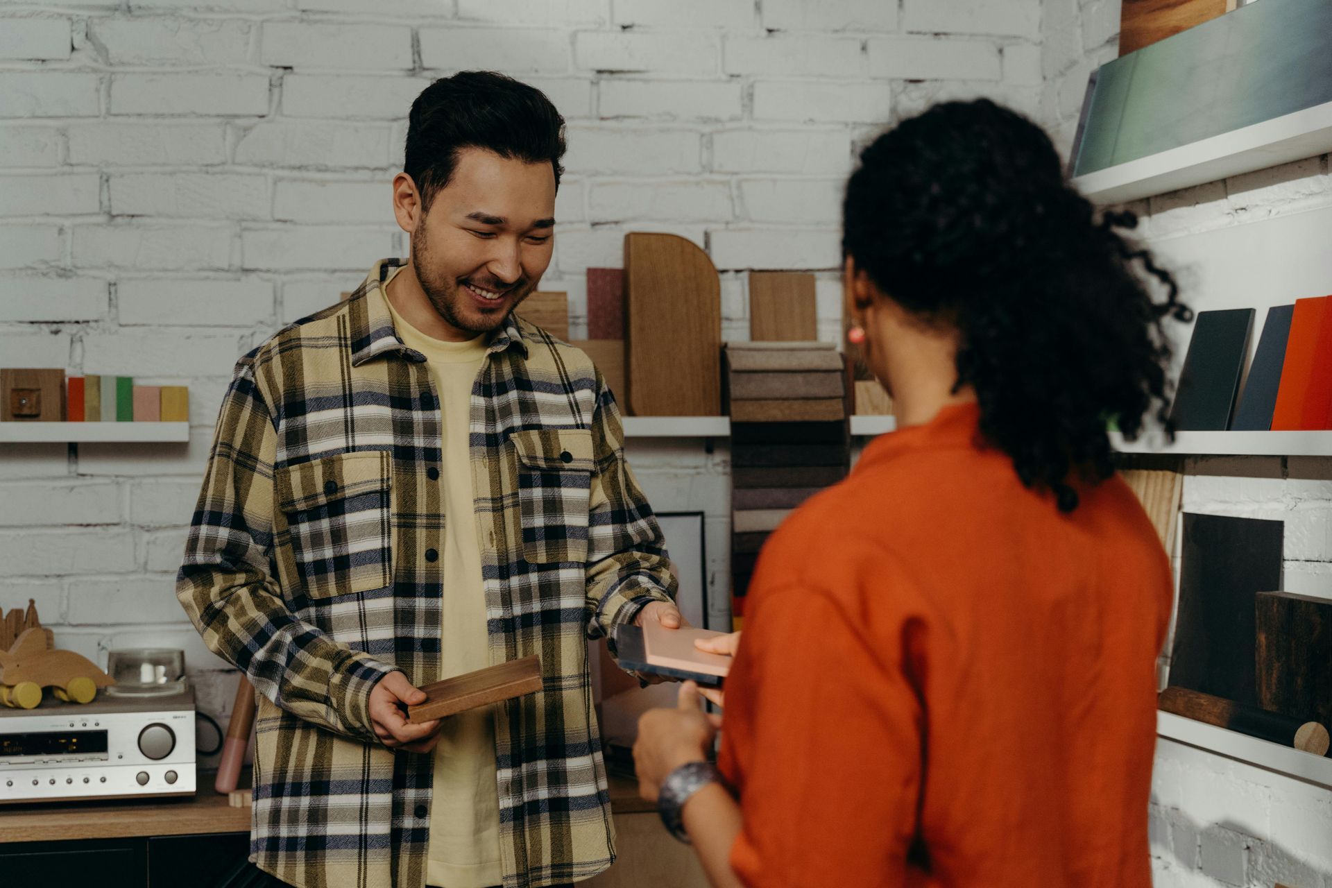 Man in plaid shirt smiling, showing wood samples to another person in a store.