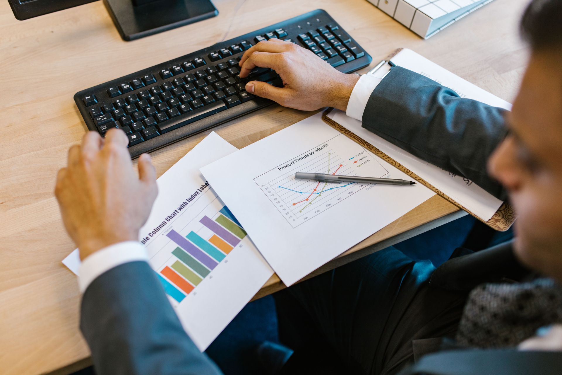 Person working at a desk with charts and graphs, using a keyboard and mouse.