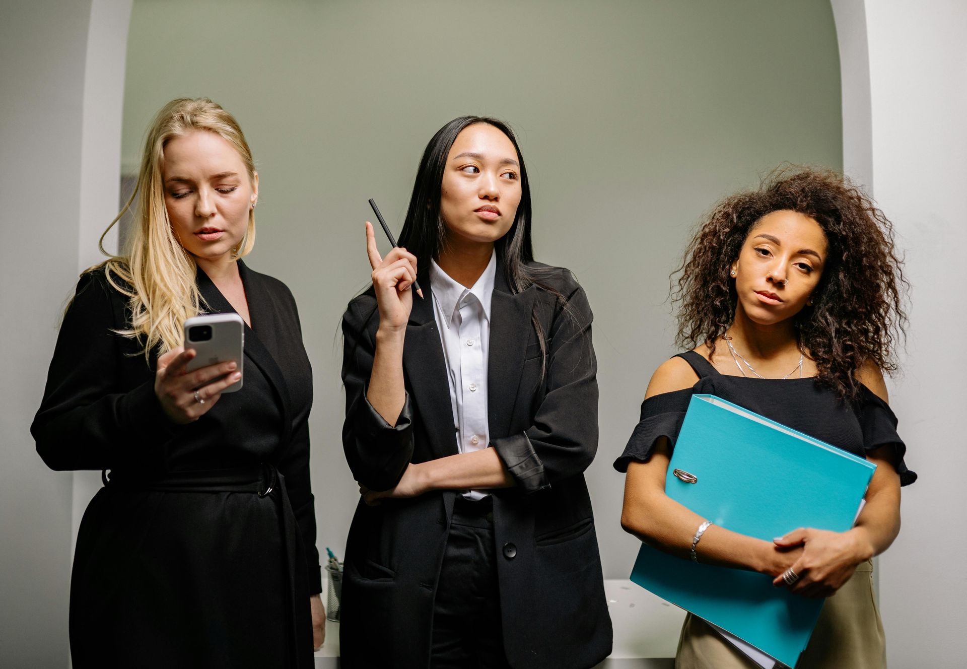 Three people in business attire, one on phone, one holding a pen, and one with a folder, looking focused.