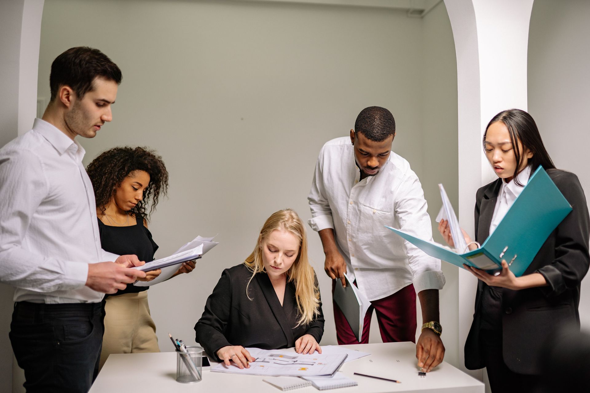 Five coworkers reviewing documents around a desk in a bright office
