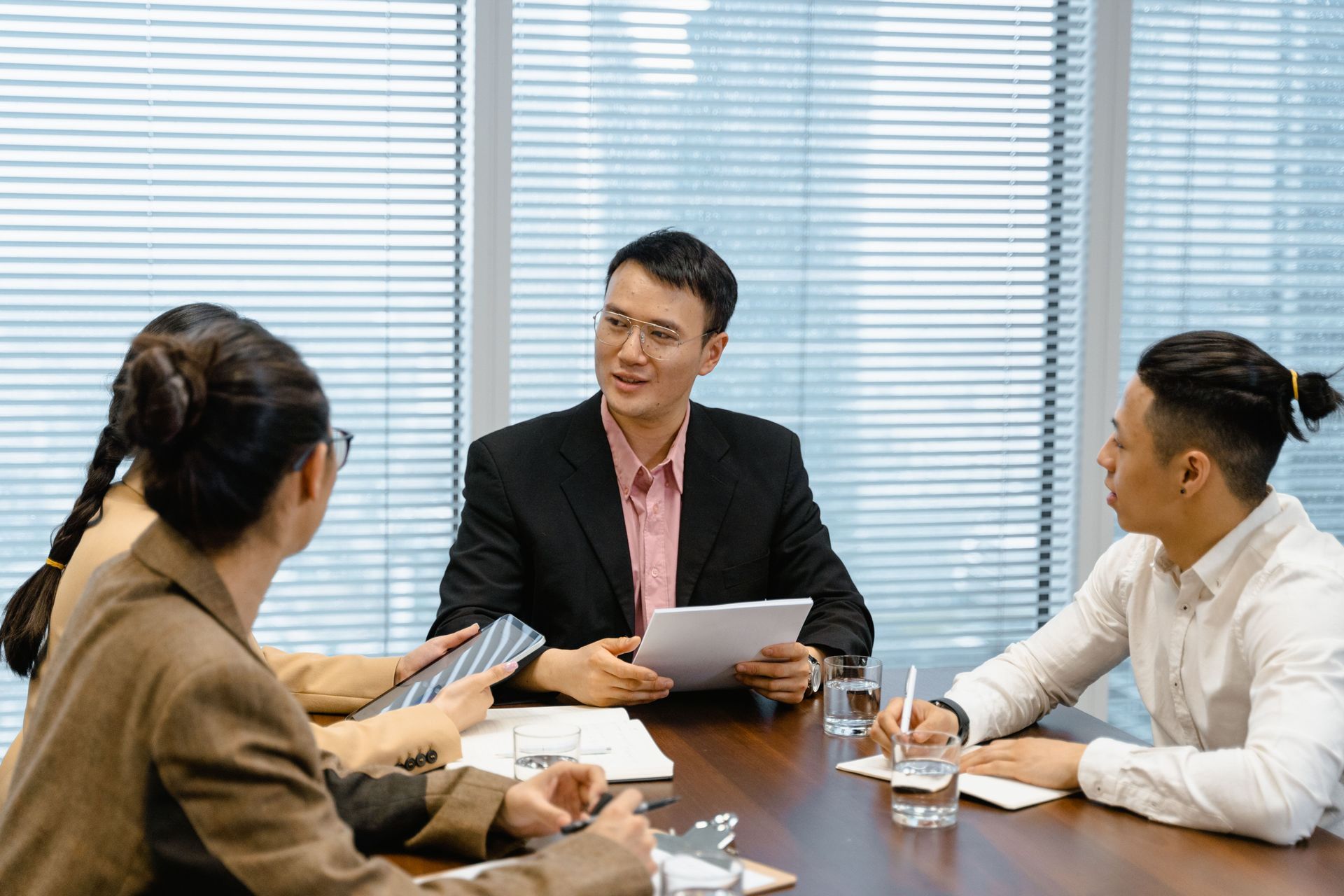 Three people in a meeting room discussing documents around a table