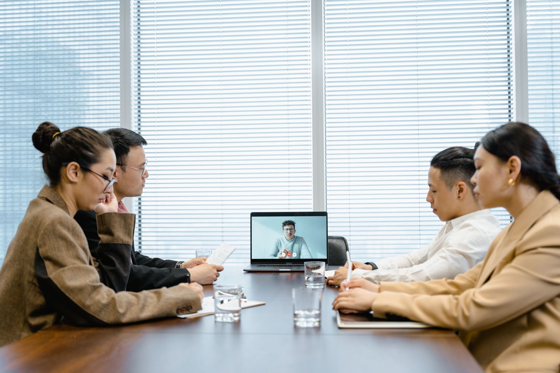 People in a conference room video meeting around a table, with a laptop centered on the screen