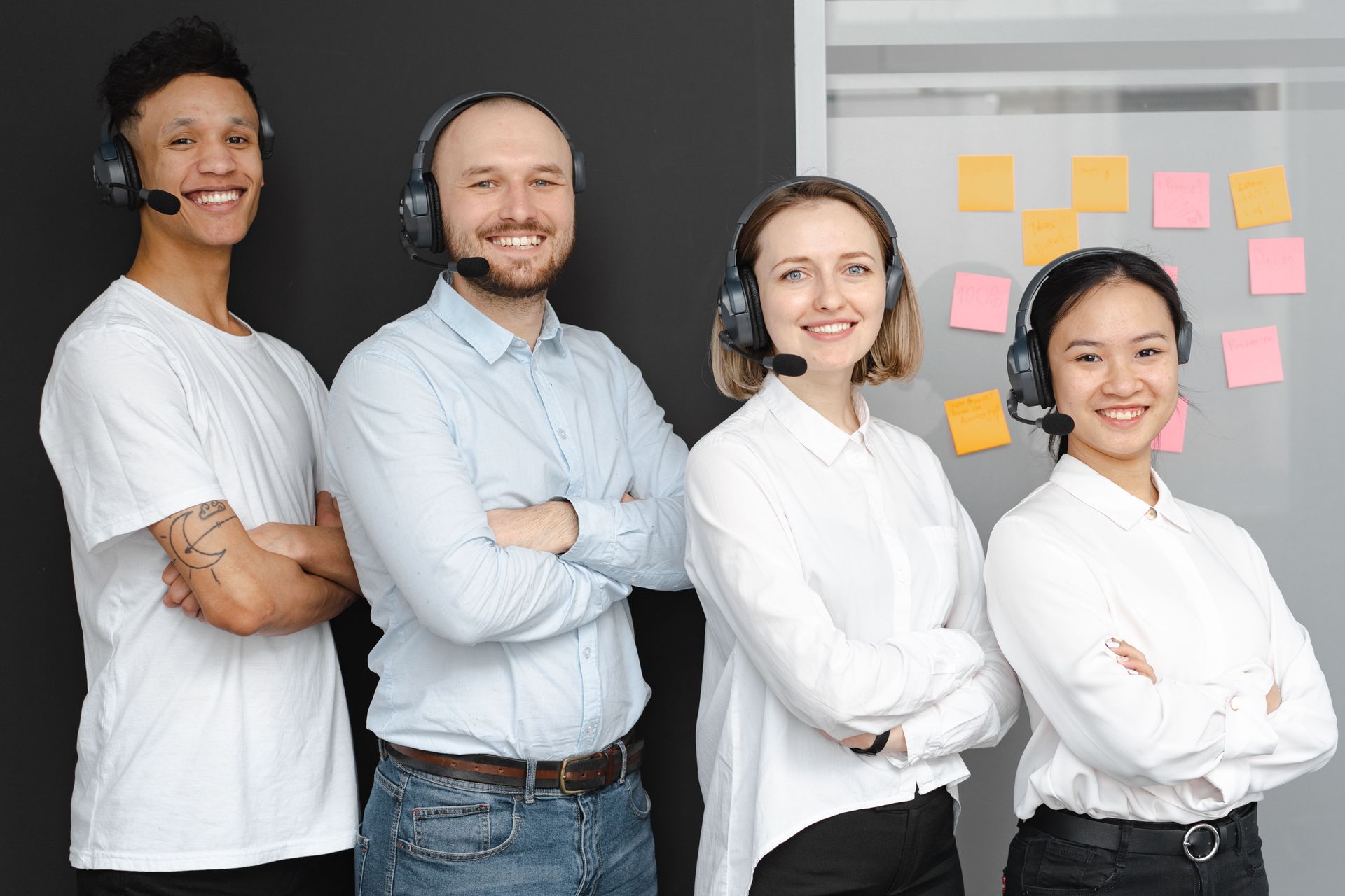 Four colleagues stand with arms crossed in a bright office, smiling in front of sticky notes.