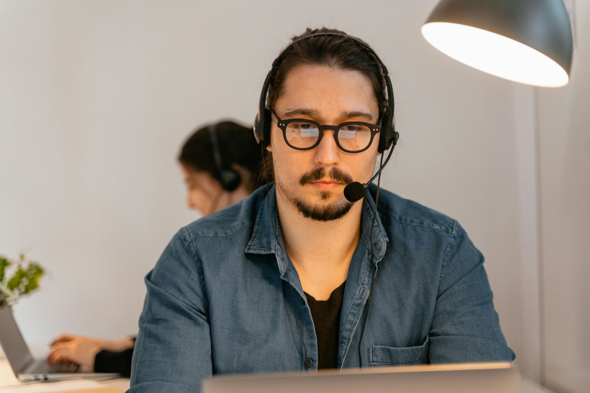 Man with headset and glasses looking at camera, working at a desk.
