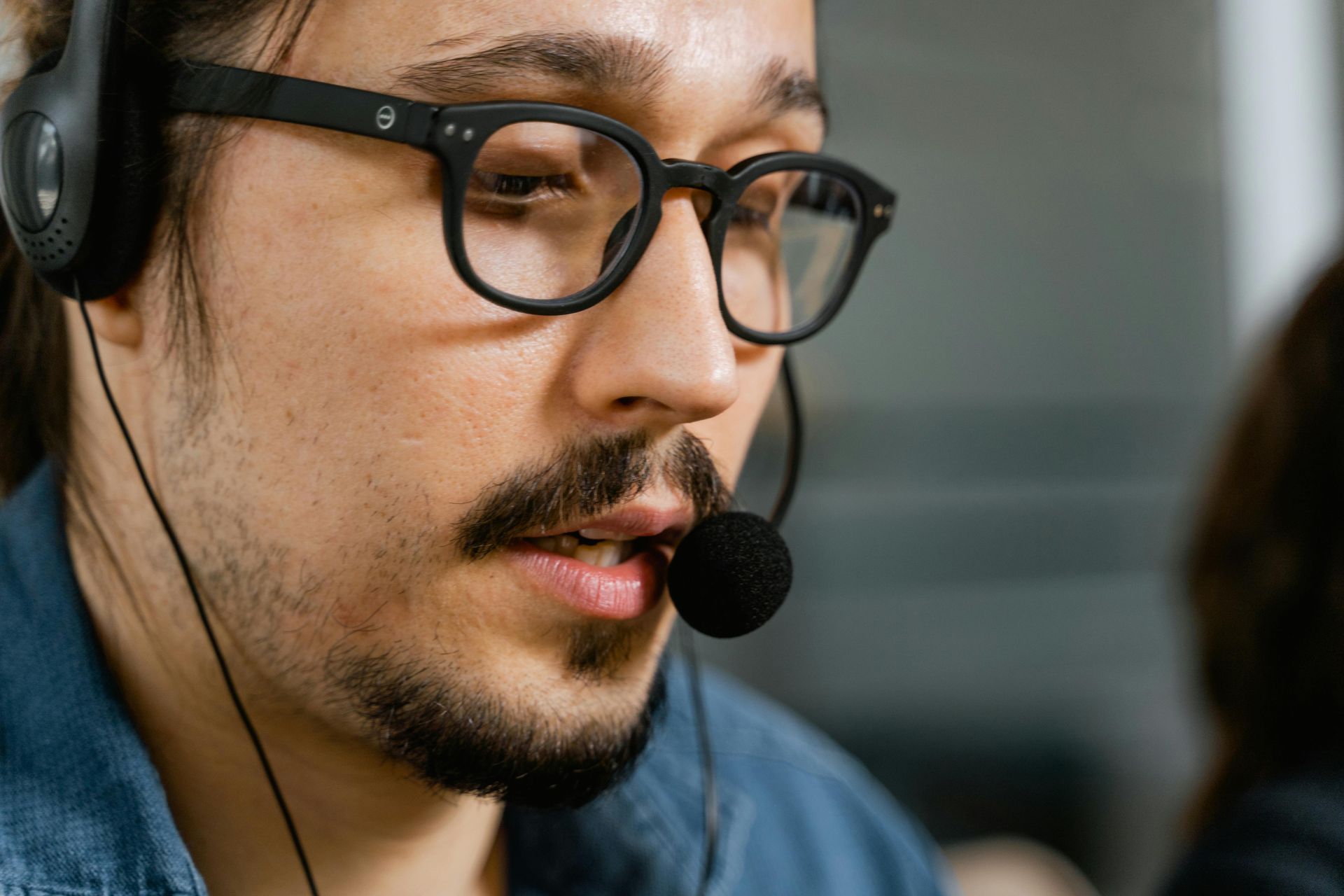 Man with glasses and headset speaks into microphone.
