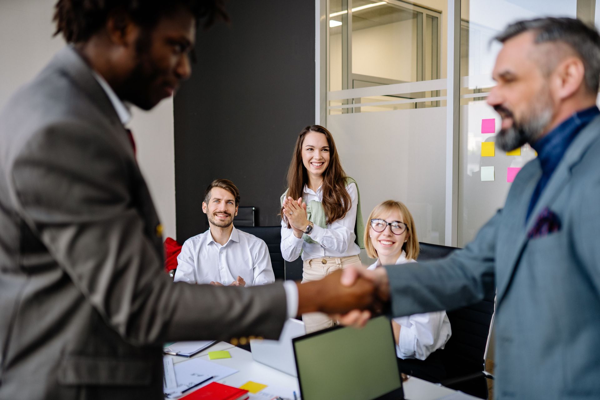 Colleagues shaking hands in a bright office during a meeting, with others smiling in the background