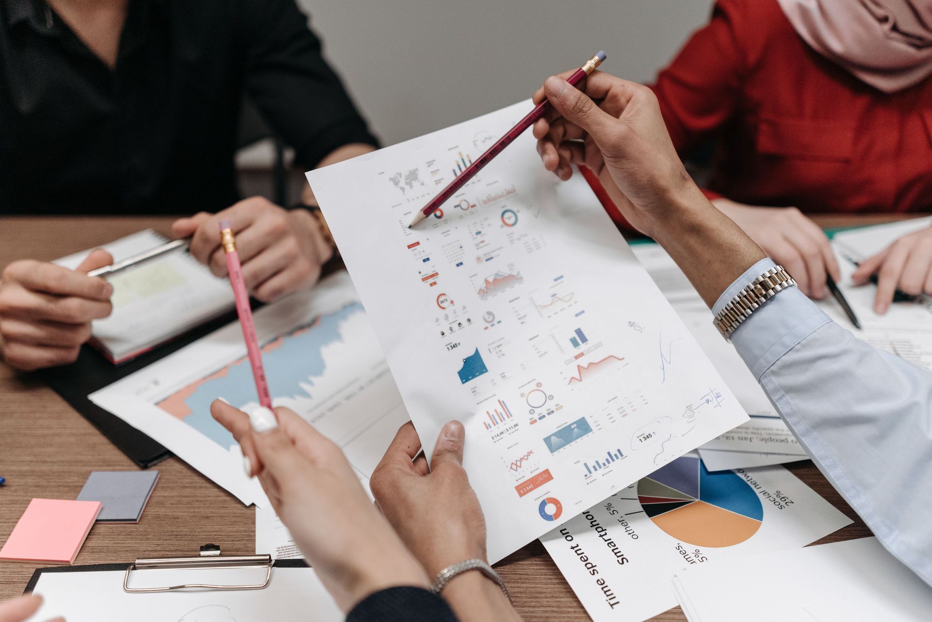 Team reviewing printed charts and graphs around a table in a meeting
