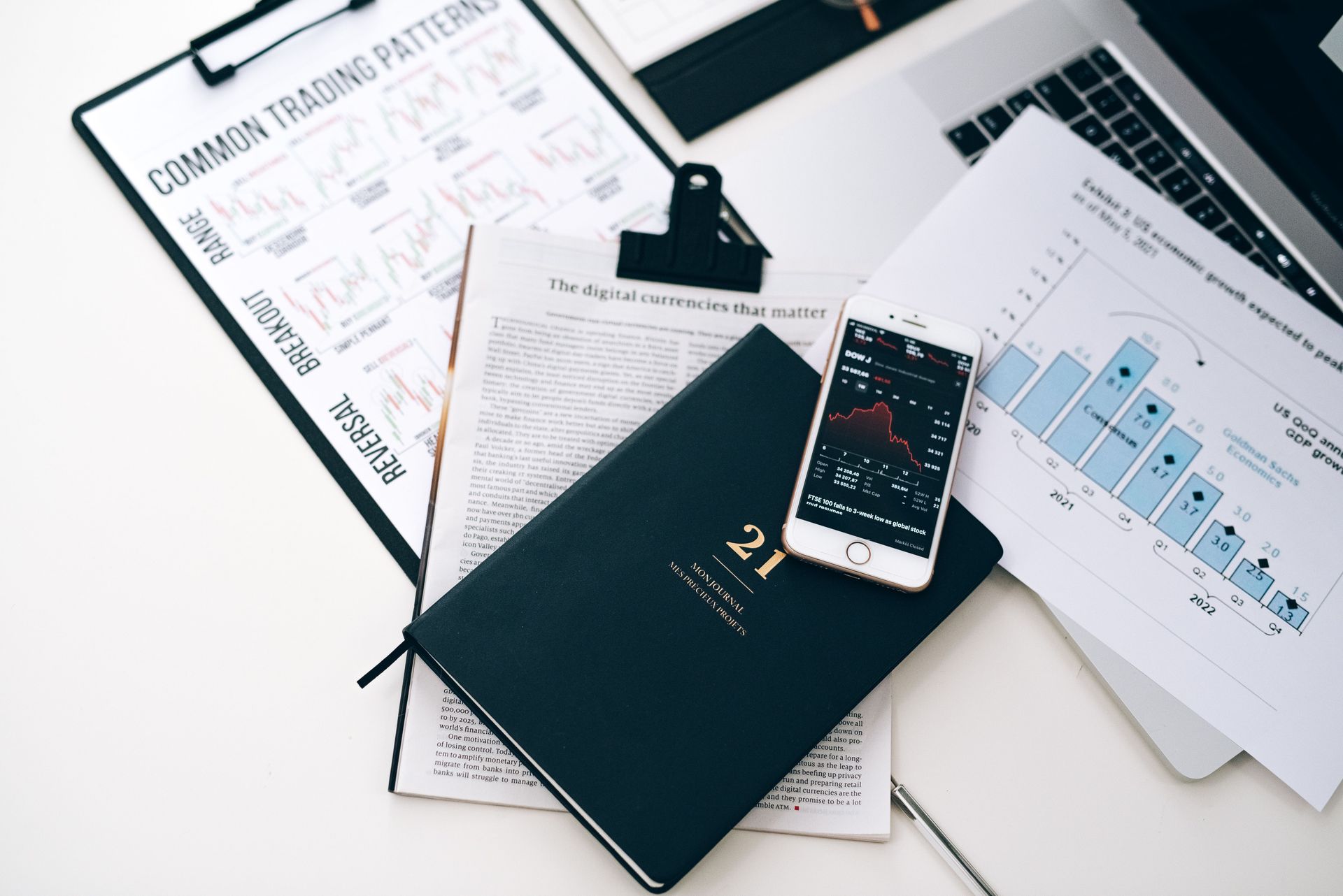 Workspace with notebooks, papers, smartphone, and tablet showing charts and notes on a white desk