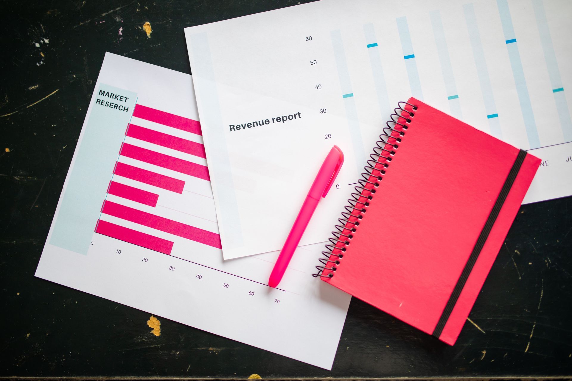 Pink notebook, pen, and charts on a desk, suggesting a business or planning workspace.