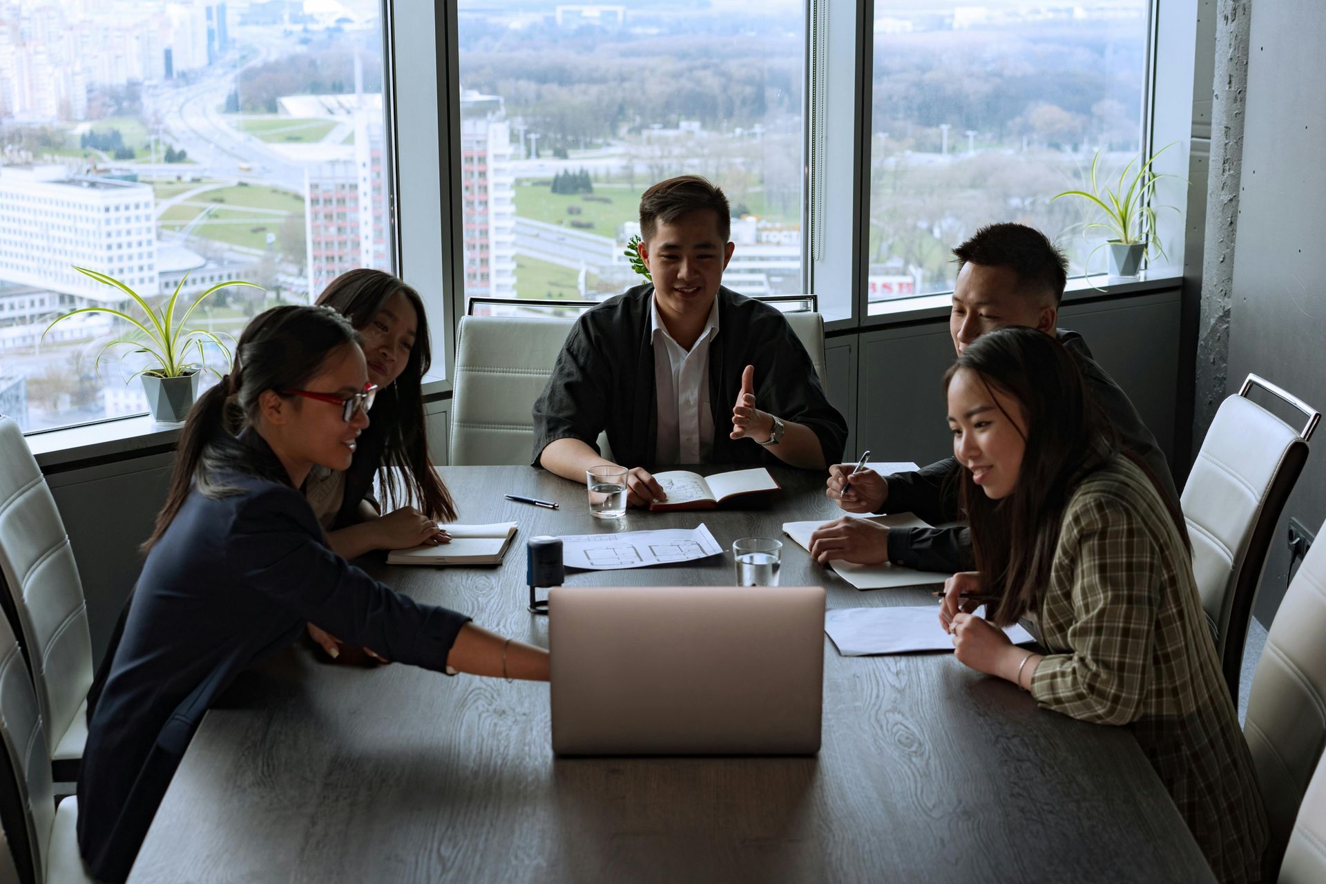 People in an office meeting around a table, looking at a laptop and documents.
