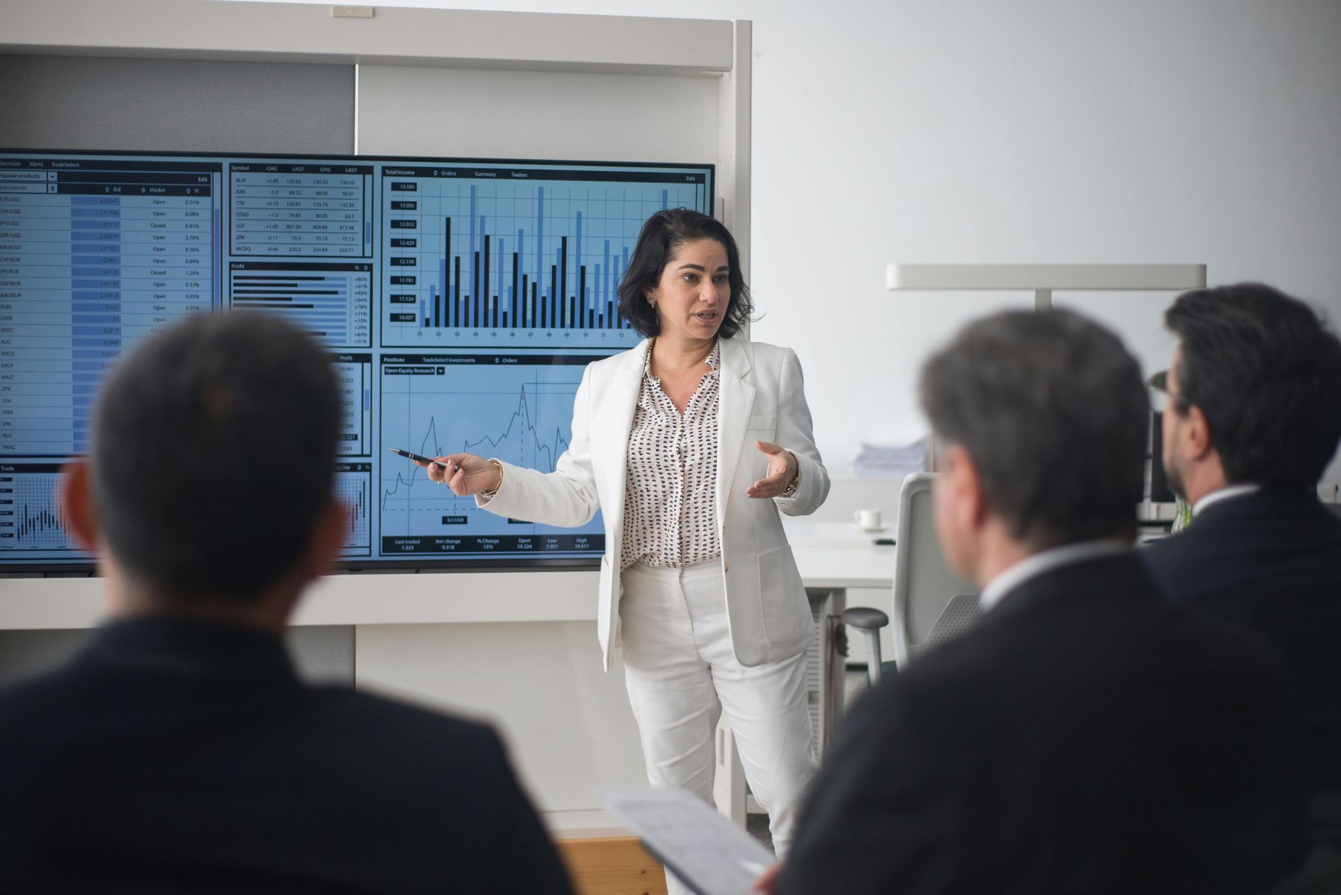 A professional presenting data on a large screen to colleagues in a brightly lit office meeting.
