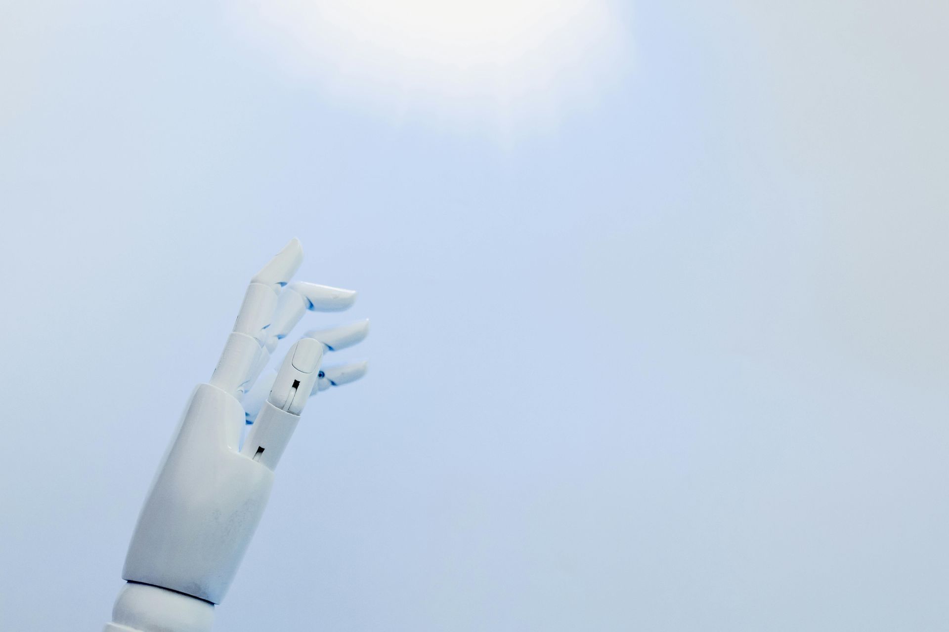 White robotic hand reaching upward toward a bright sky