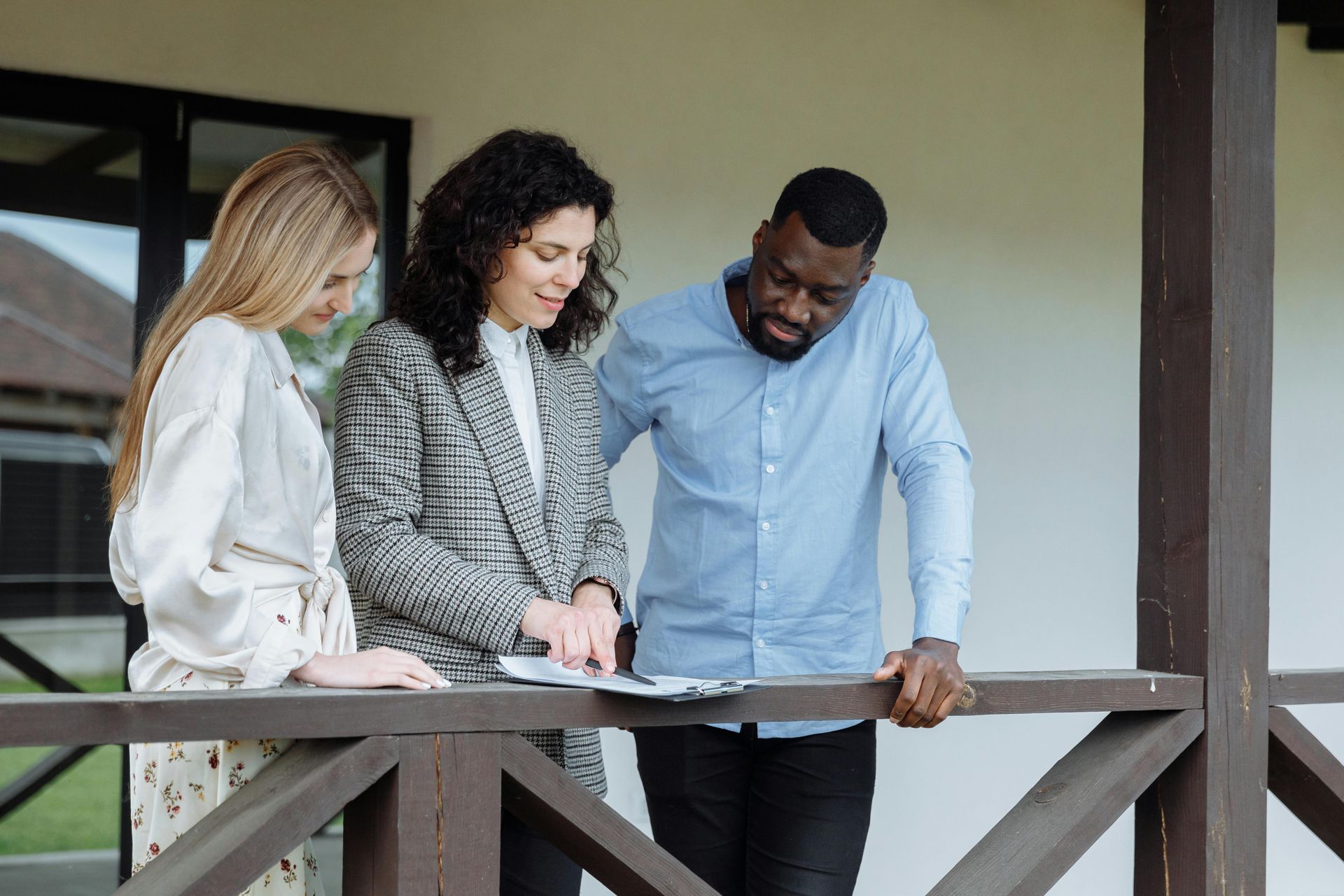 Three people stand on a porch, reviewing documents together outside a building.