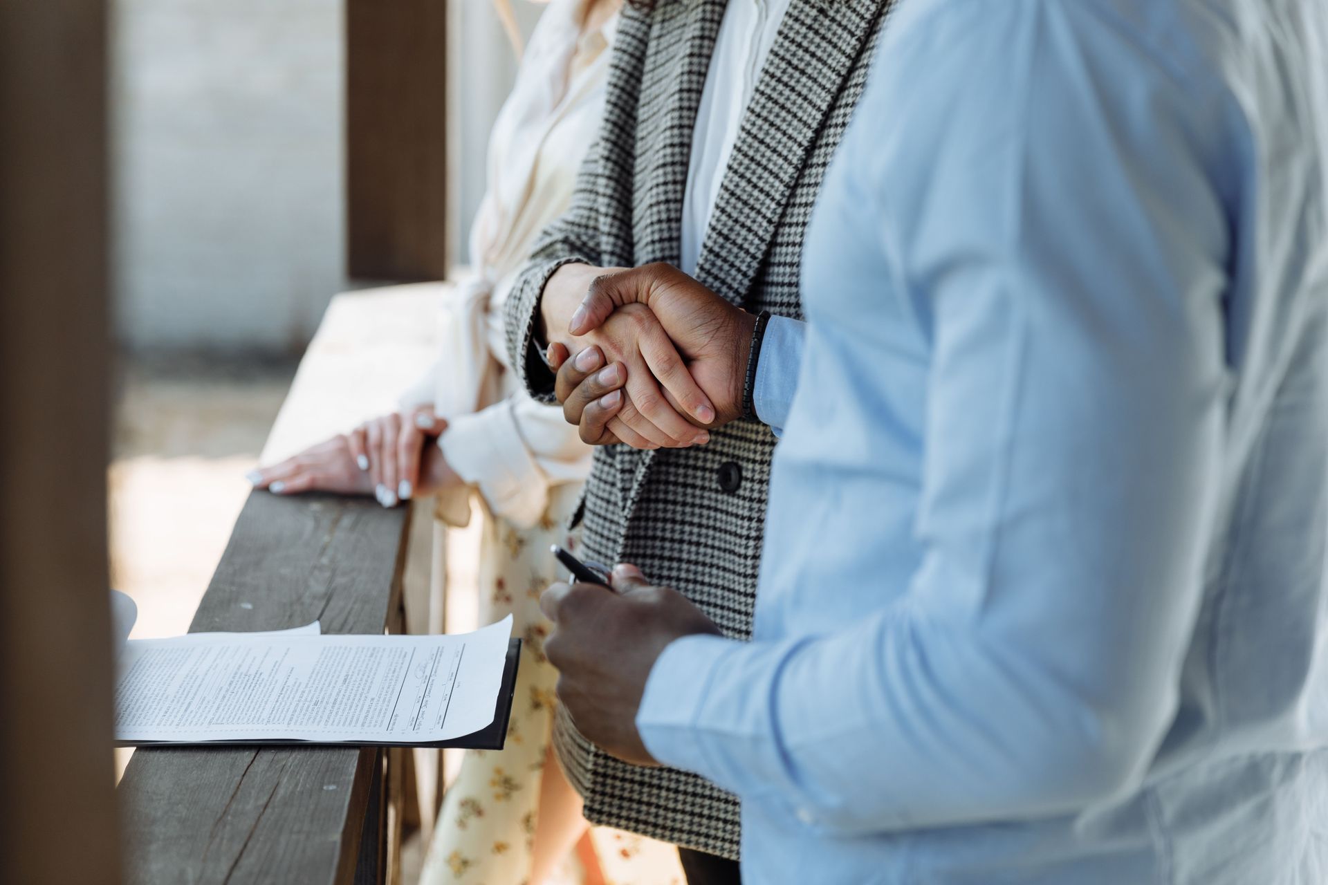Two people leaning on a railing, holding hands, with a paper on the ledge outdoors.