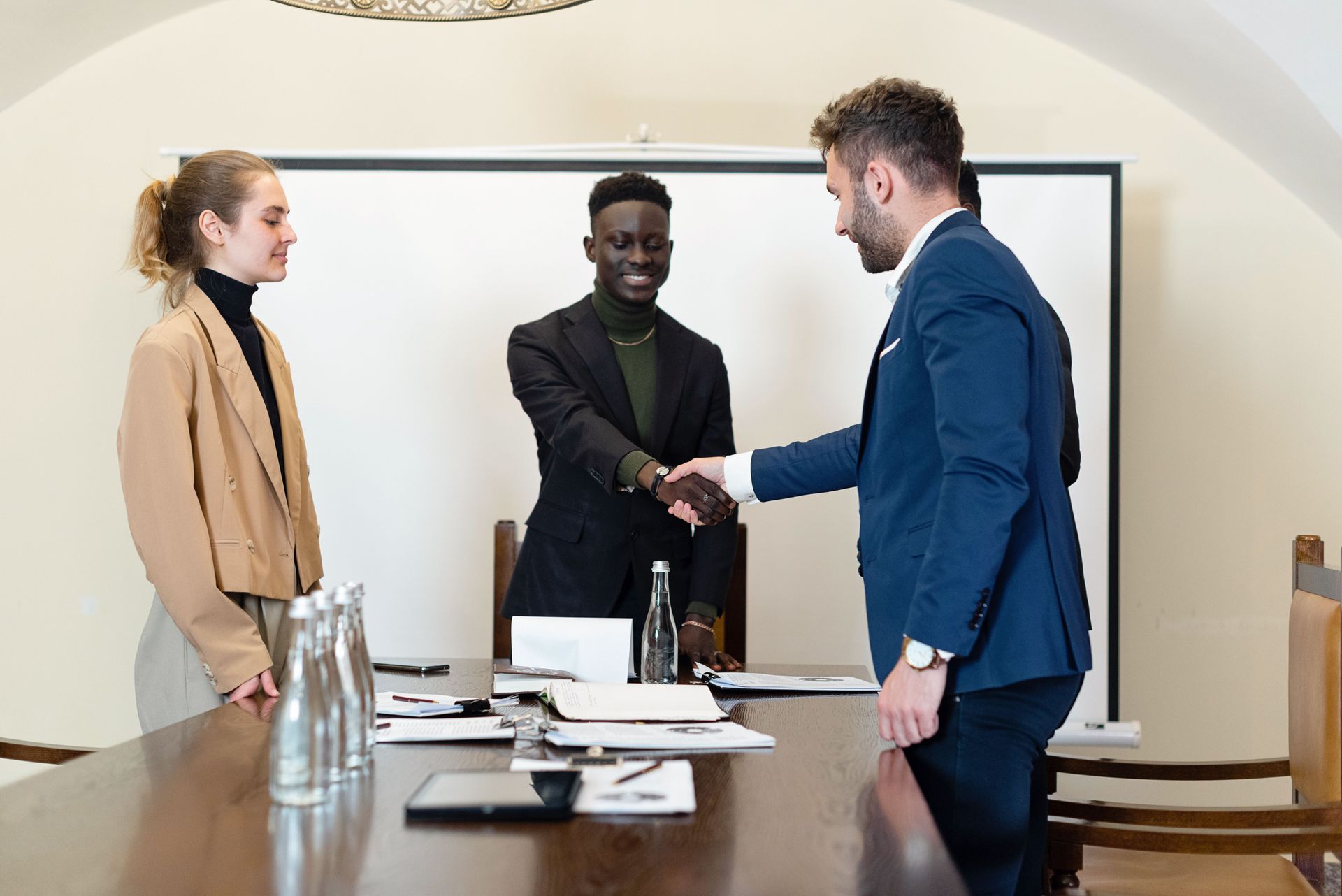 Three people shaking hands across a conference table in a meeting room
