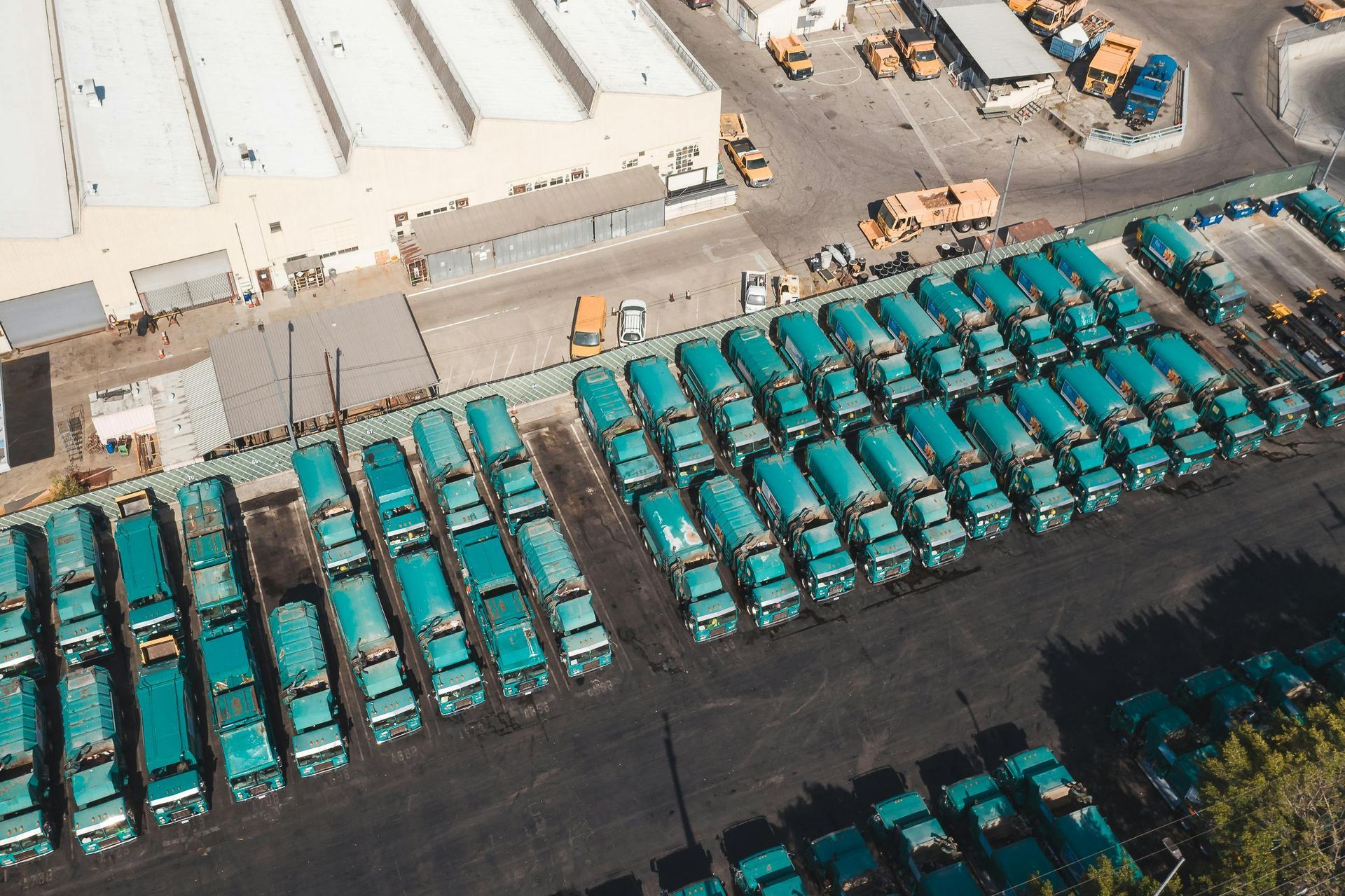 An aerial view of a large lot packed with rows of identical teal-colored industrial cement mixer trucks.