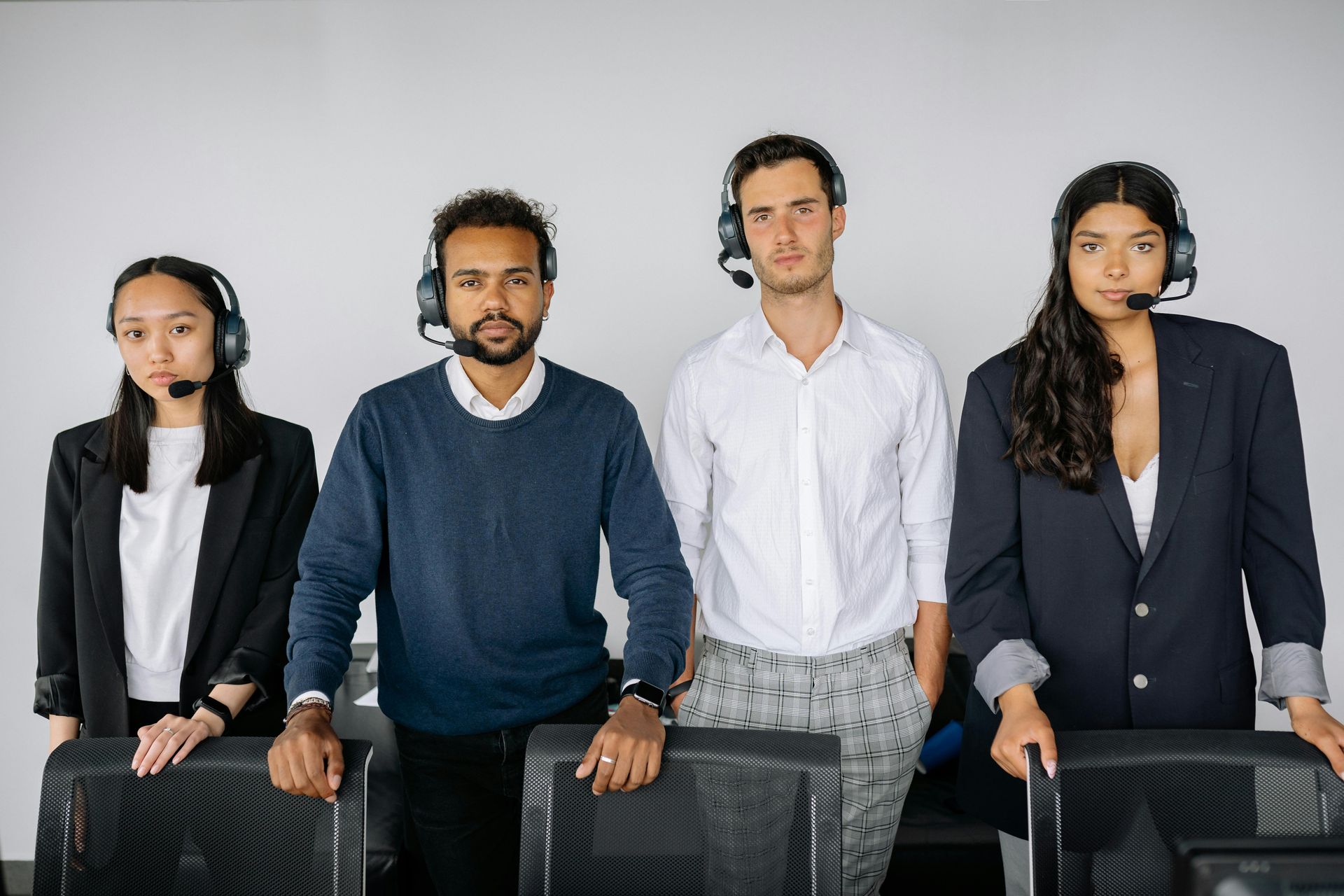 Four people wearing headsets and professional attire stand in a row in a bright office space.