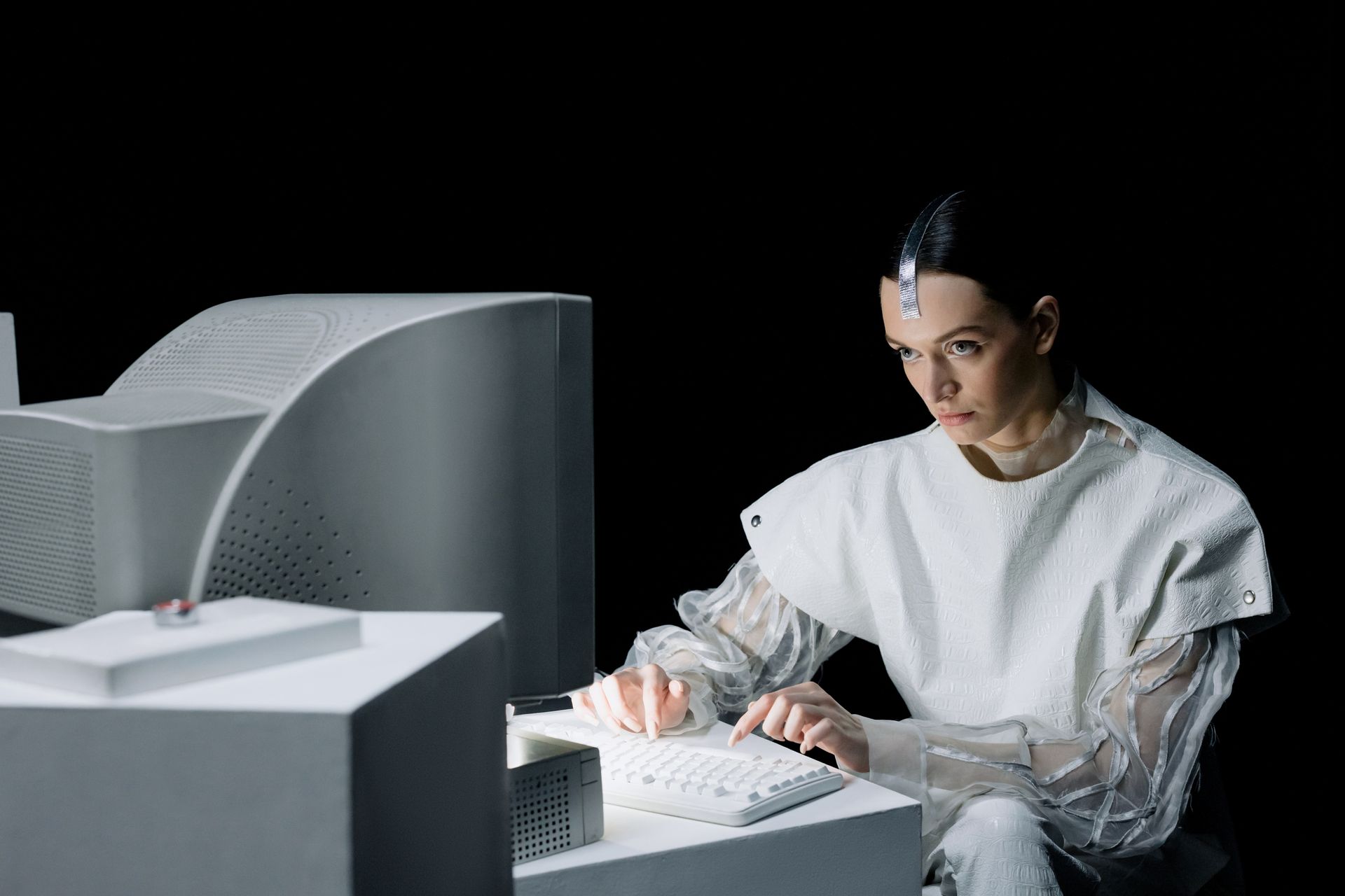 Person in white shirt typing at a computer in a dark room with a large monitor.