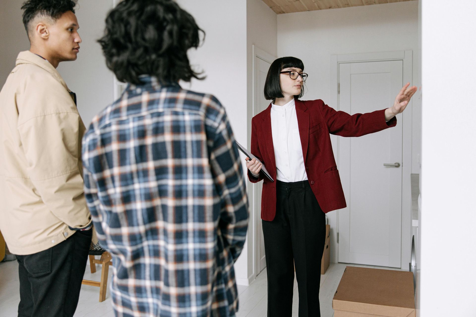 Real estate agent shows a couple a room, pointing towards a wall.