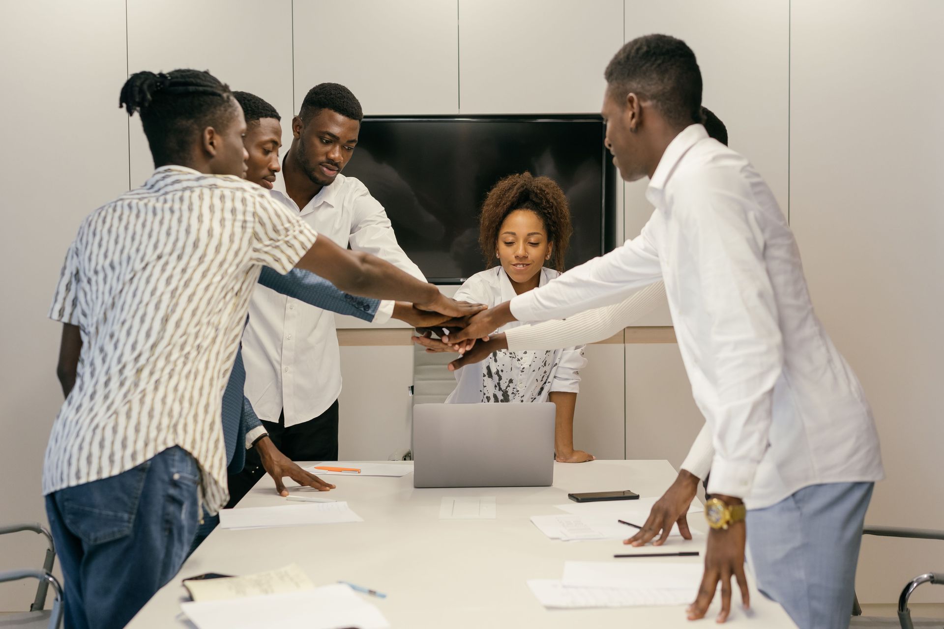 Team of coworkers stacking hands over a laptop in a bright conference room