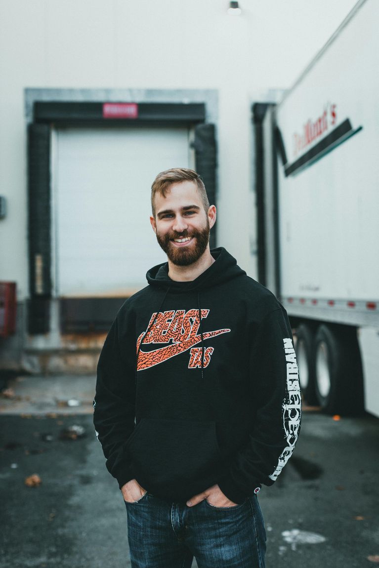 Man in black Nike hoodie smiles, standing outside a loading dock.