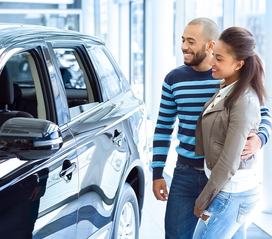 A man and a woman are standing next to a car in a showroom.