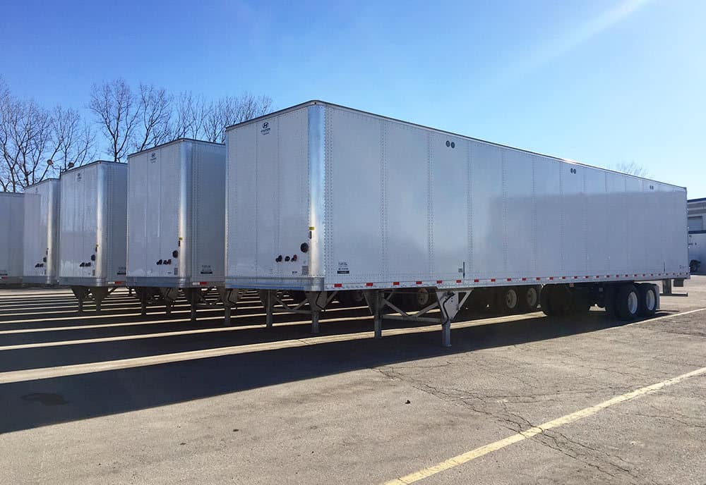 A row of white semi trailers are parked in a parking lot.
