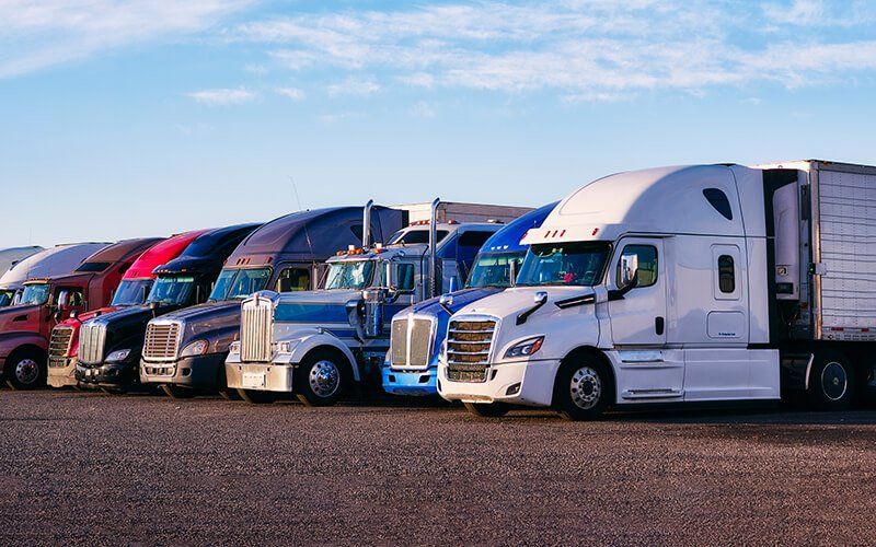 A row of semi trucks are parked in a parking lot.