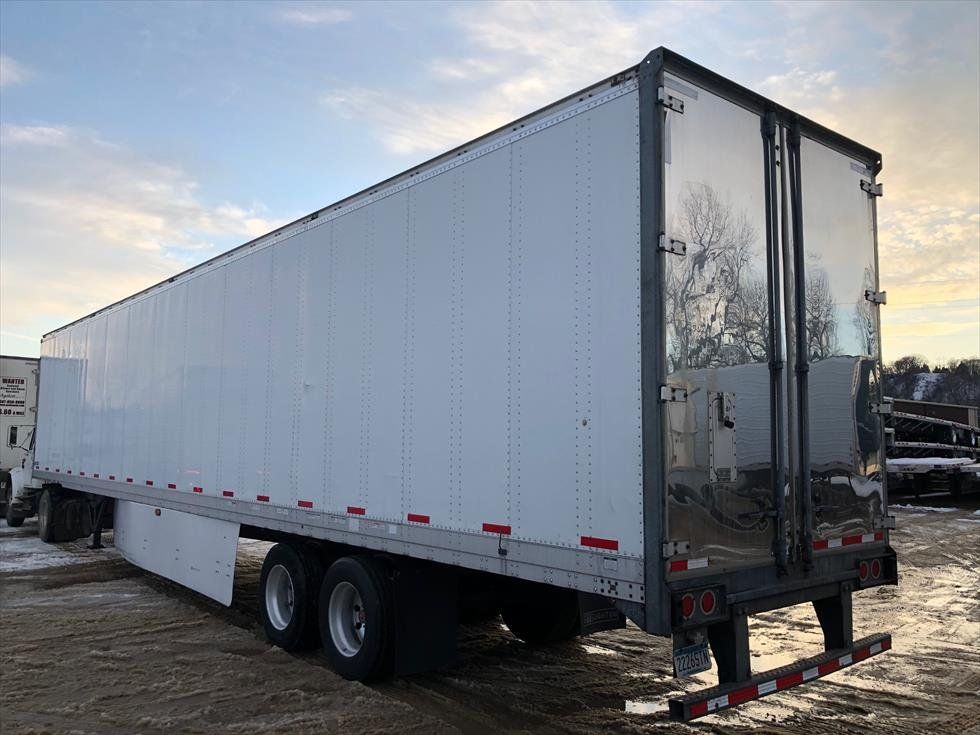 A white semi trailer is parked in a dirt field.