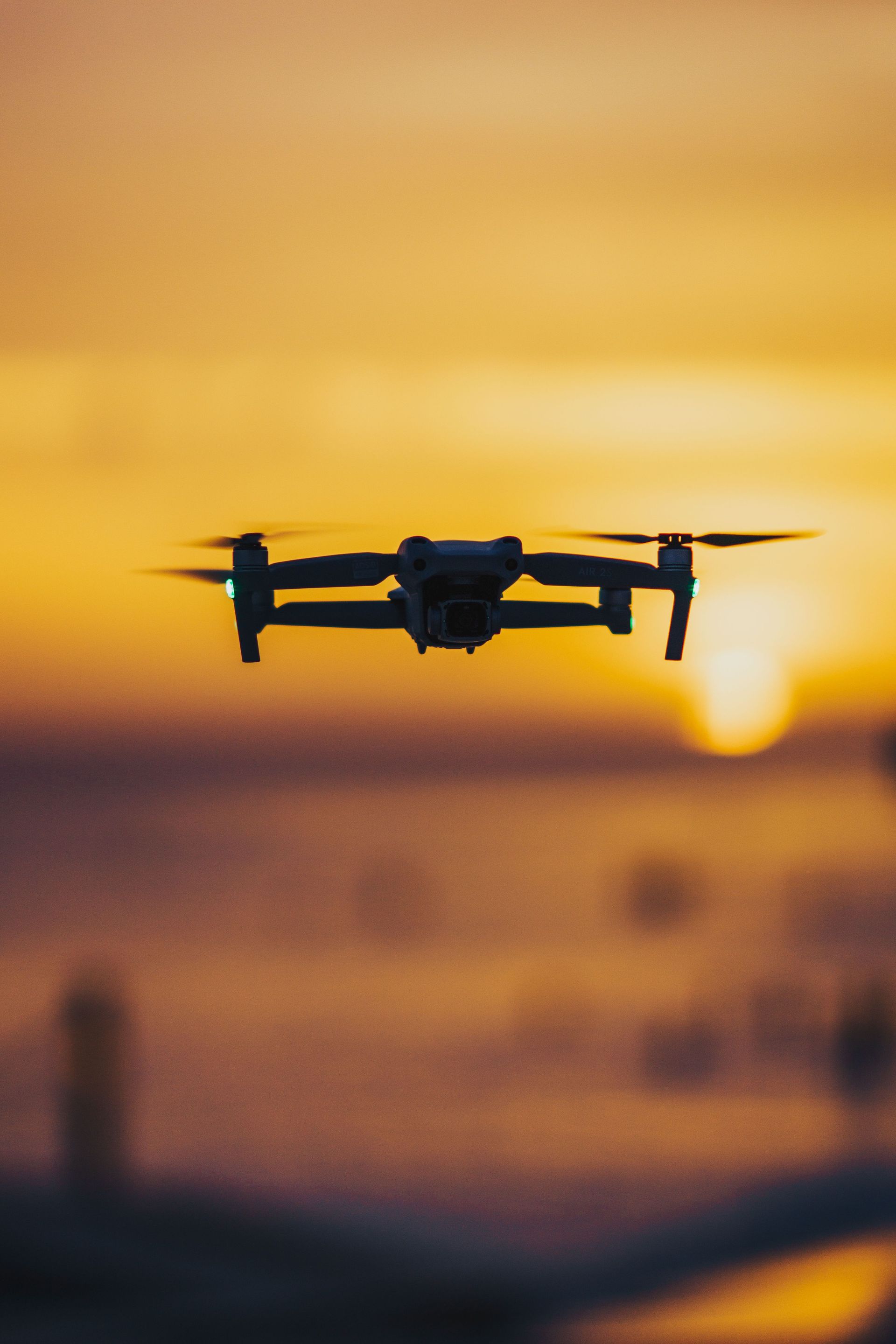 Drone silhouetted against a golden sunset sky, hovering above a blurred landscape