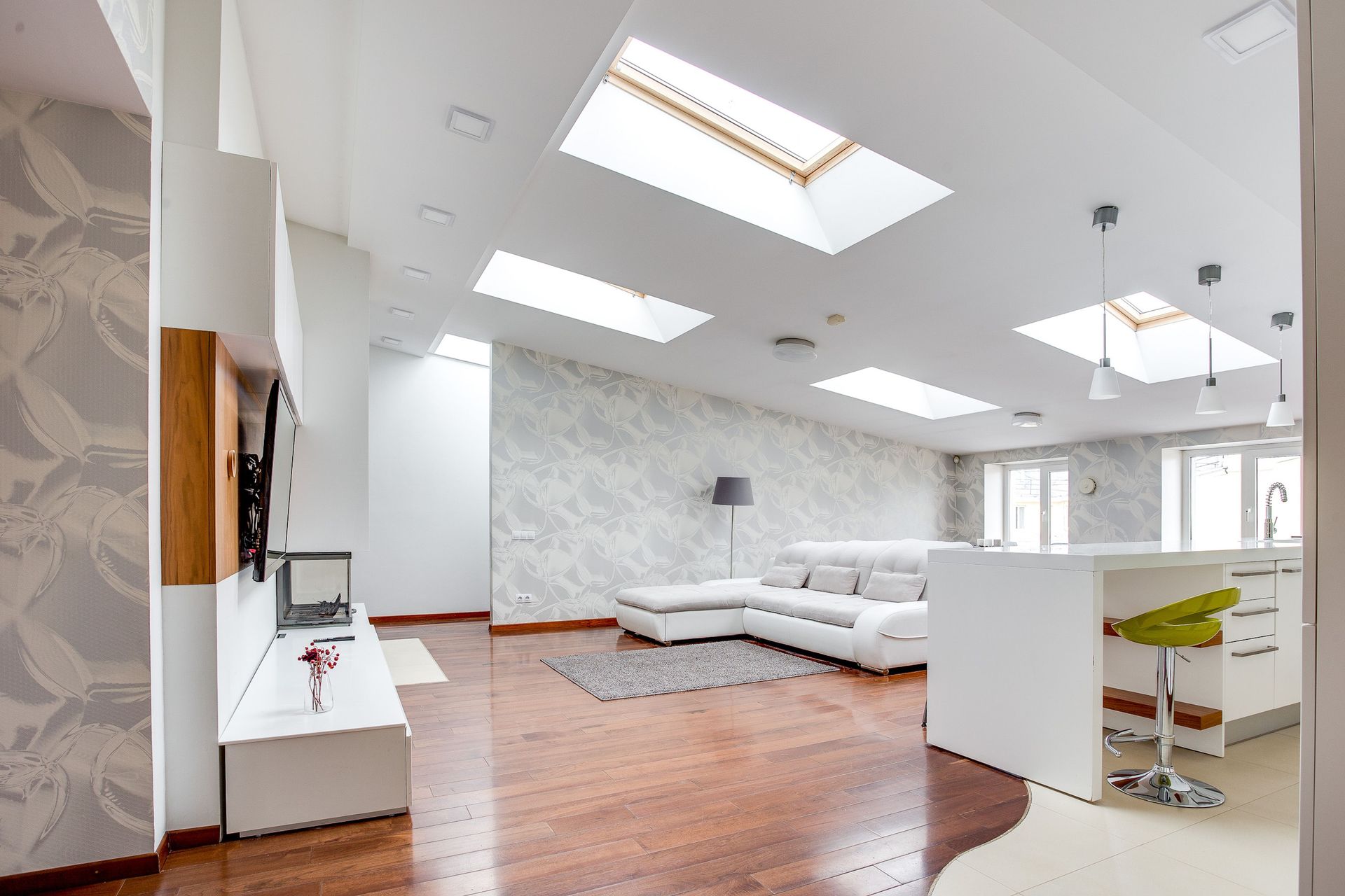 Bright modern living room with white sofas, skylights, hardwood floors, and a minimalist staircase