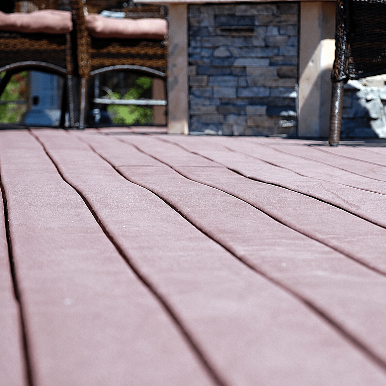 Wooden deck boards leading to a stone wall and benches on a patio
