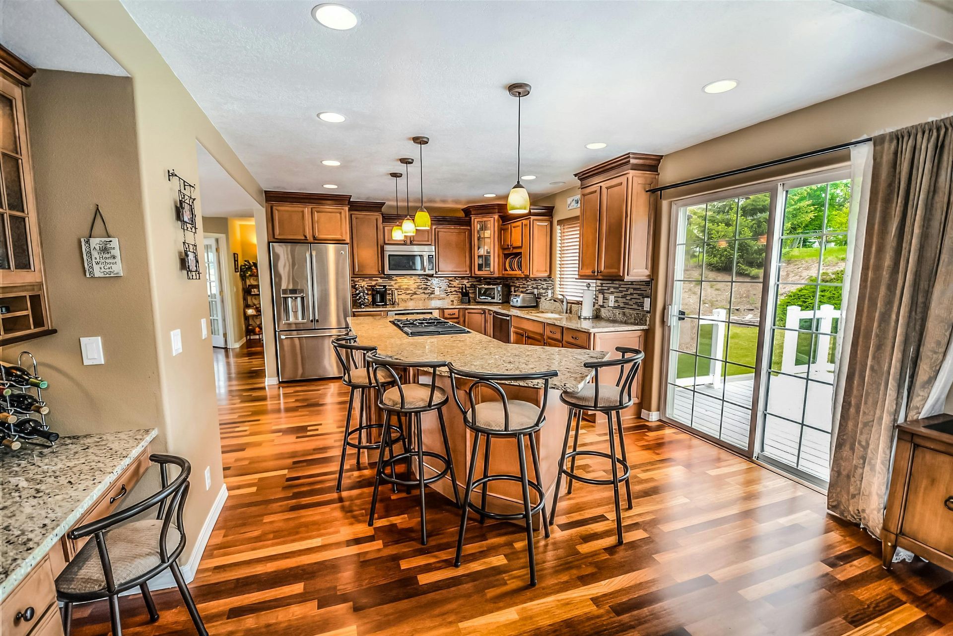 A modern kitchen with wood cabinets, granite countertops, an island with four bar stools, and sliding glass patio doors.