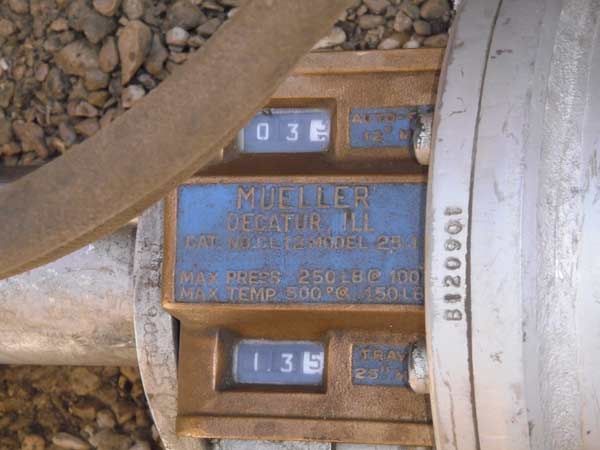 Close-up of a blue gas meter with digital readouts and metal piping outdoors.