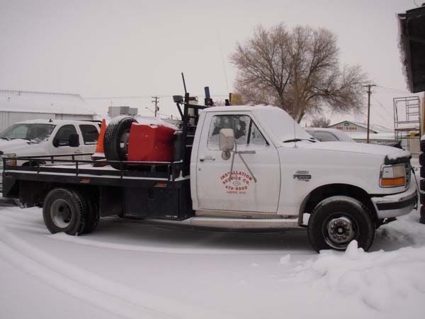 White utility pickup truck with red tank equipment parked in a snowy lot