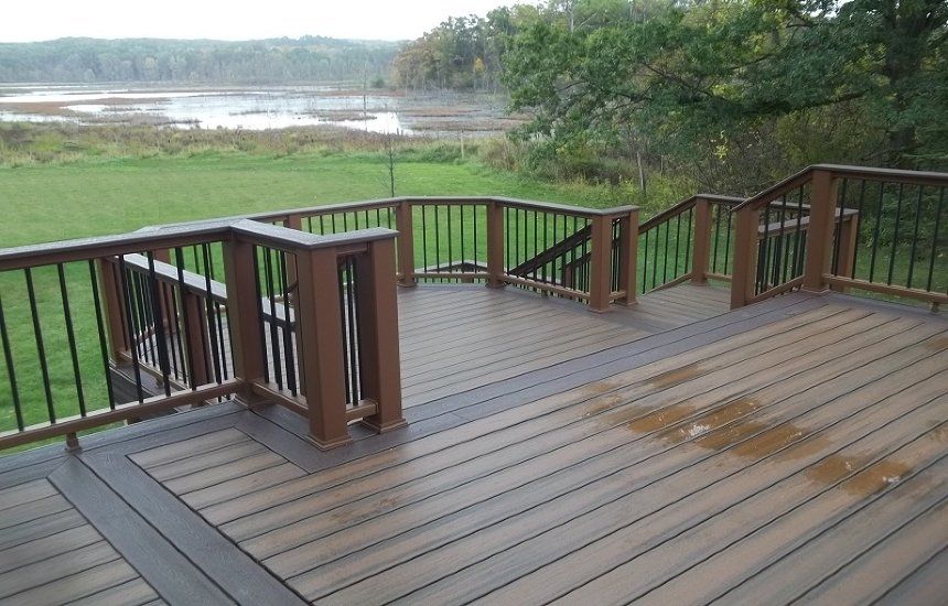 Wooden deck overlooking a grassy shoreline and lake, with railings and wet spots on the boards.
